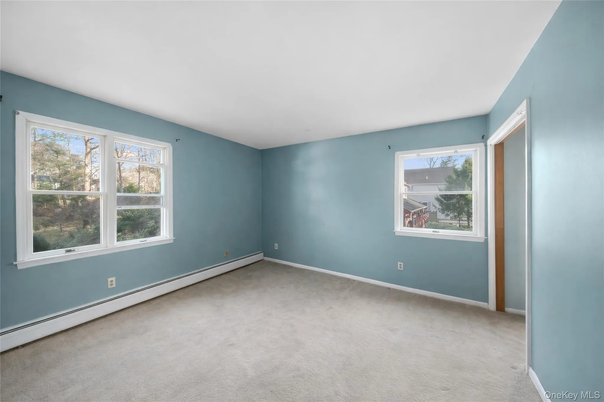 Room featuring light blue walls, gray carpet, white baseboards, and multiple windows with white trim Room featuring light blue walls, gray carpet, white baseboards, and multiple windows with white trim