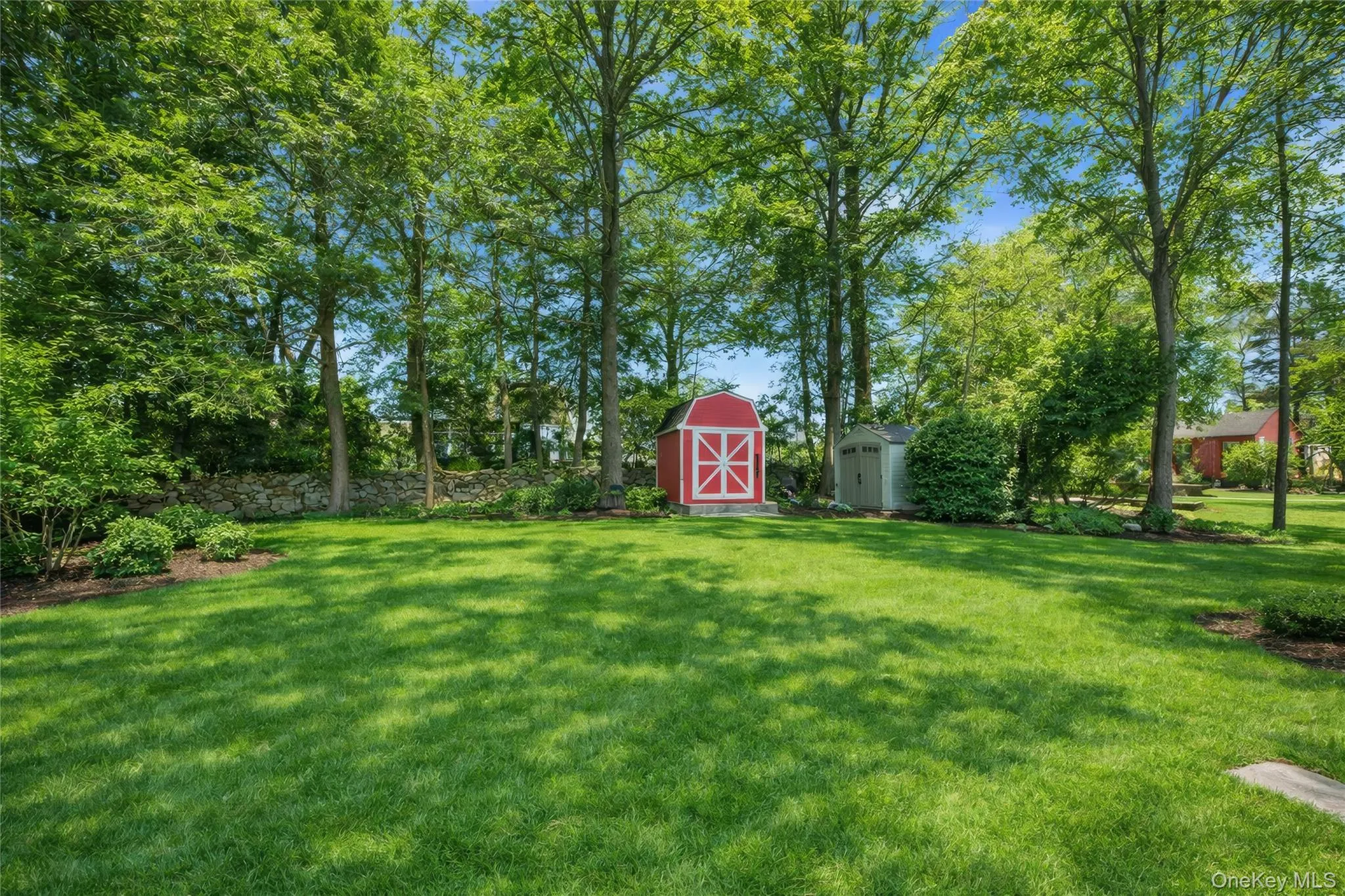 Spacious lawn area framed by mature deciduous trees and a stone retaining wall Spacious lawn area framed by mature deciduous trees and a stone retaining wall