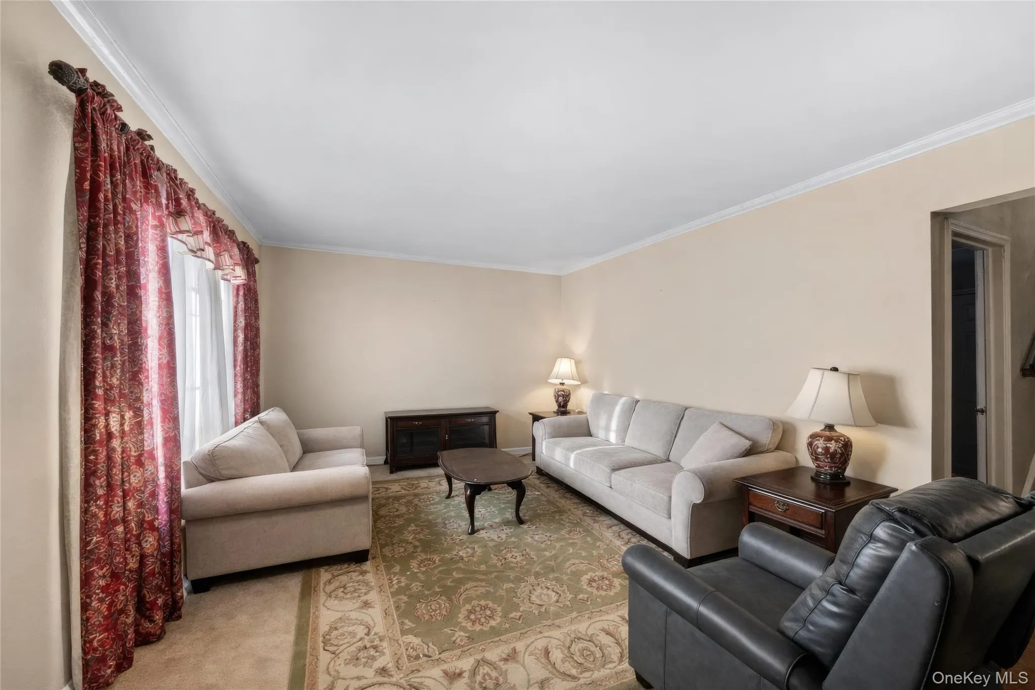 Living area featuring light-toned walls, crown molding, a window with decorative valance, and wall-to-wall carpeting Living area featuring light-toned walls, crown molding, a window with decorative valance, and wall-to-wall carpeting
