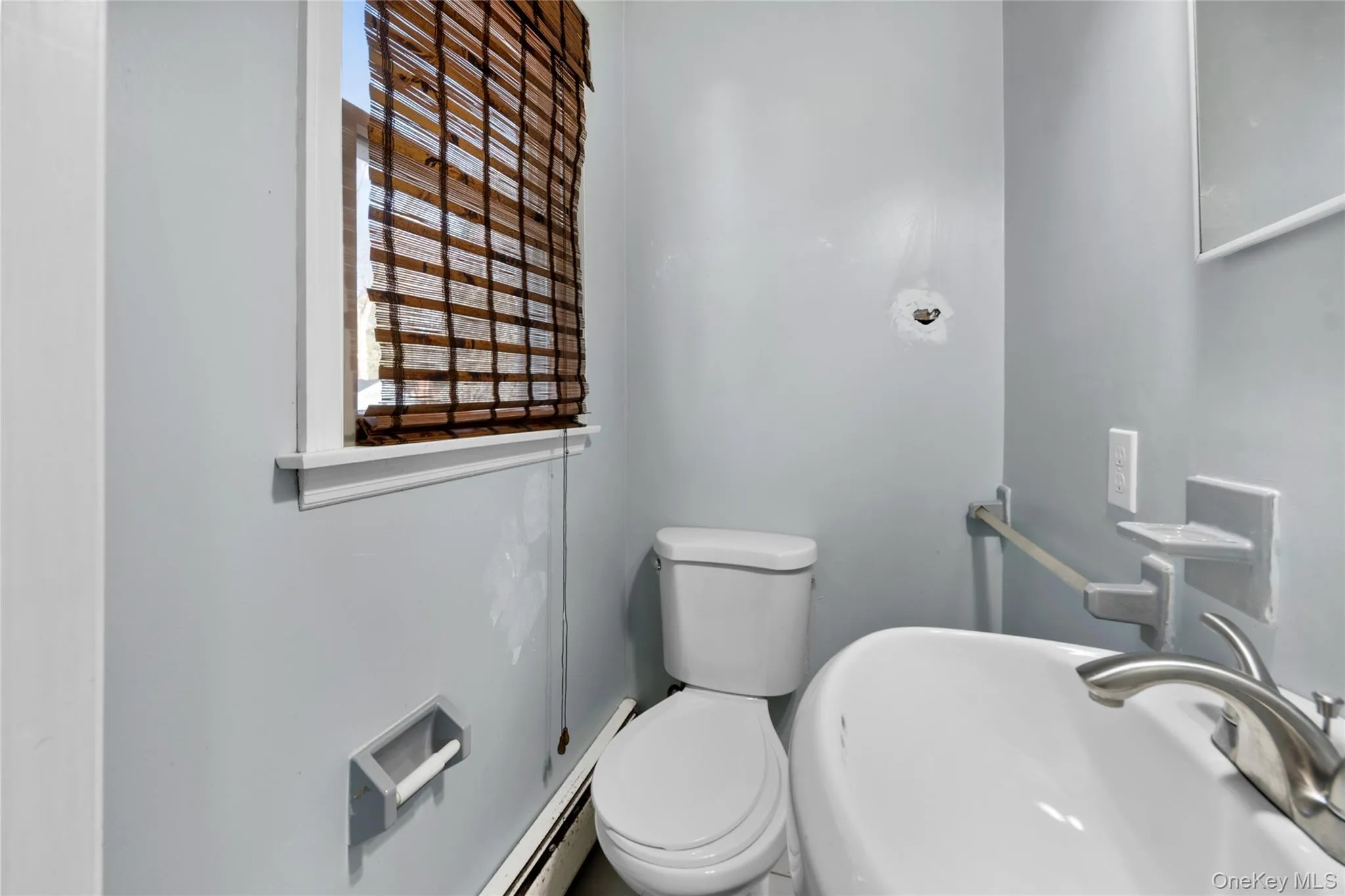 Bathroom featuring a white toilet, white pedestal sink with brushed nickel faucet, and a window with wood-slat blinds Bathroom featuring a white toilet, white pedestal sink with brushed nickel faucet, and a window with wood-slat blinds