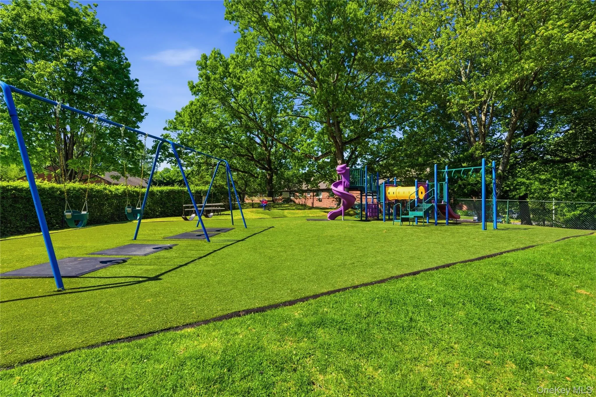 Community playground featuring multiple swing sets, a colorful play structure with slides, and monkey bars Community playground featuring multiple swing sets, a colorful play structure with slides, and monkey bars