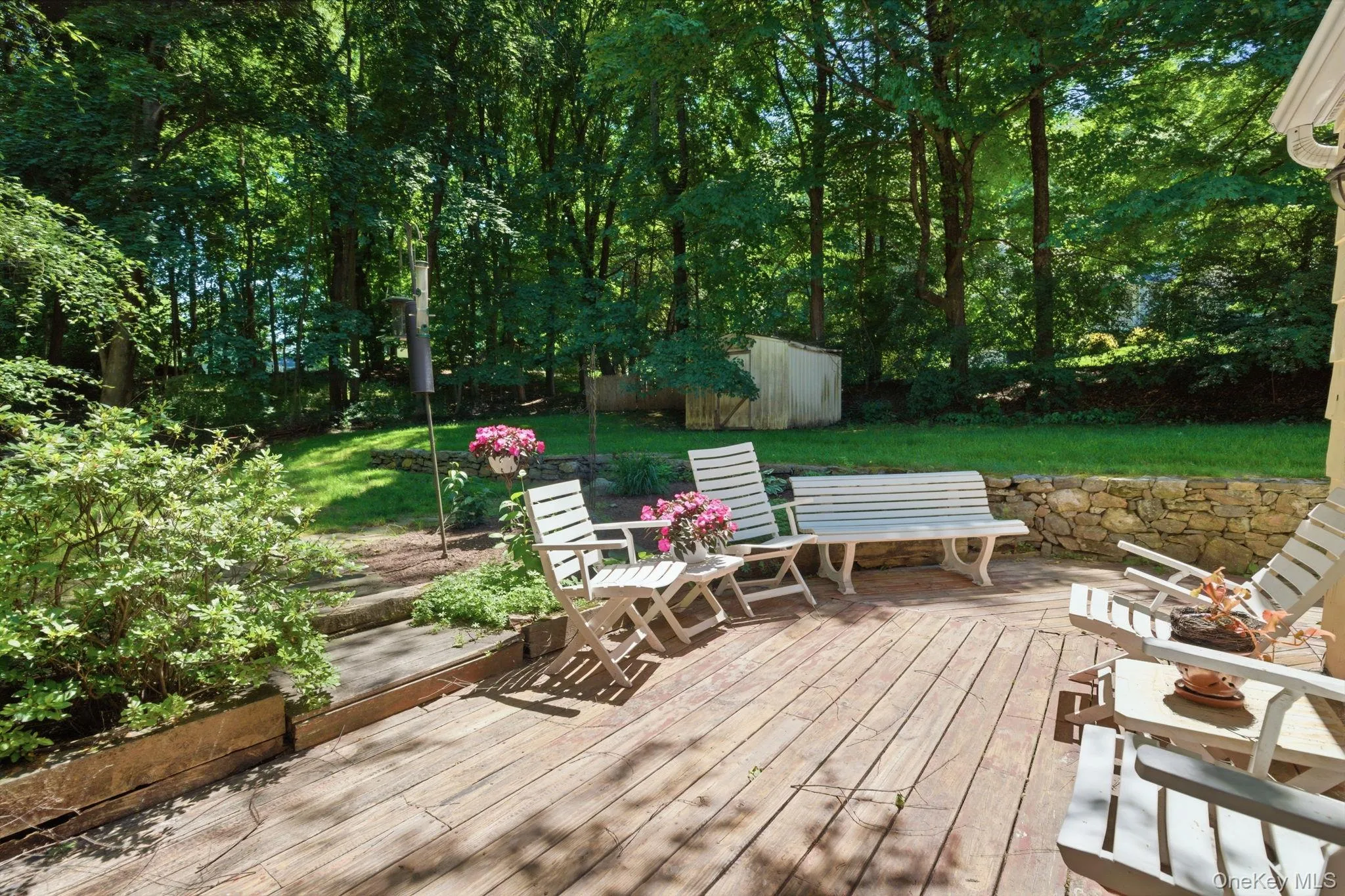 A spacious deck overlooks the backyard with a stone wall border and wooded privacy beyond. A spacious deck overlooks the backyard with a stone wall border and wooded privacy beyond.