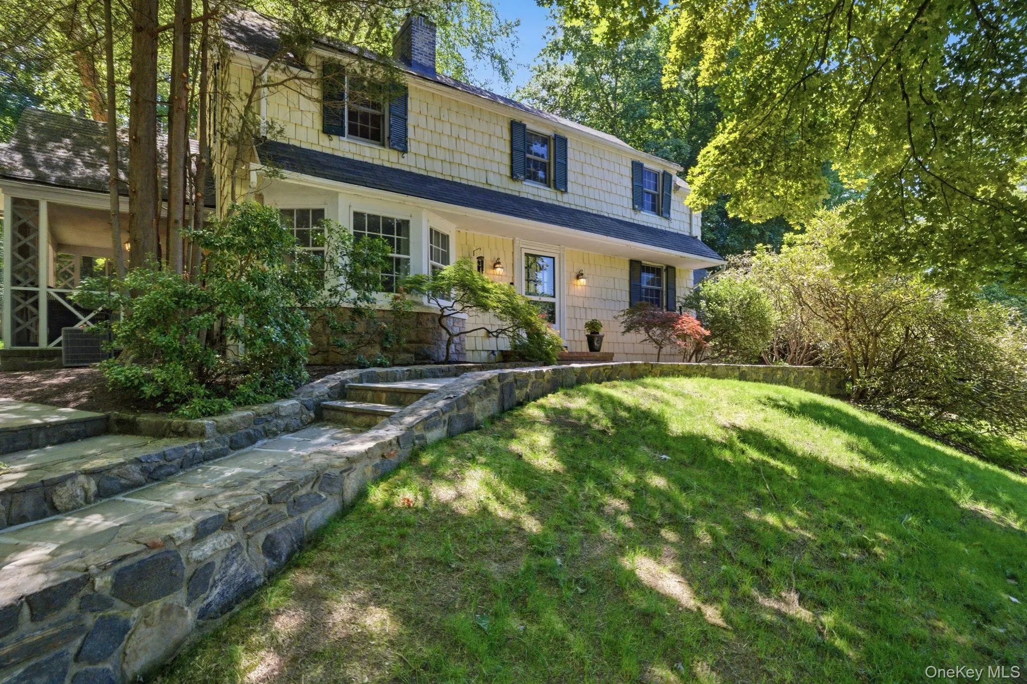 Stone steps and mature landscaping lead to the front door, with the screened porch visible to the side. Stone steps and mature landscaping lead to the front door, with the screened porch visible to the side.