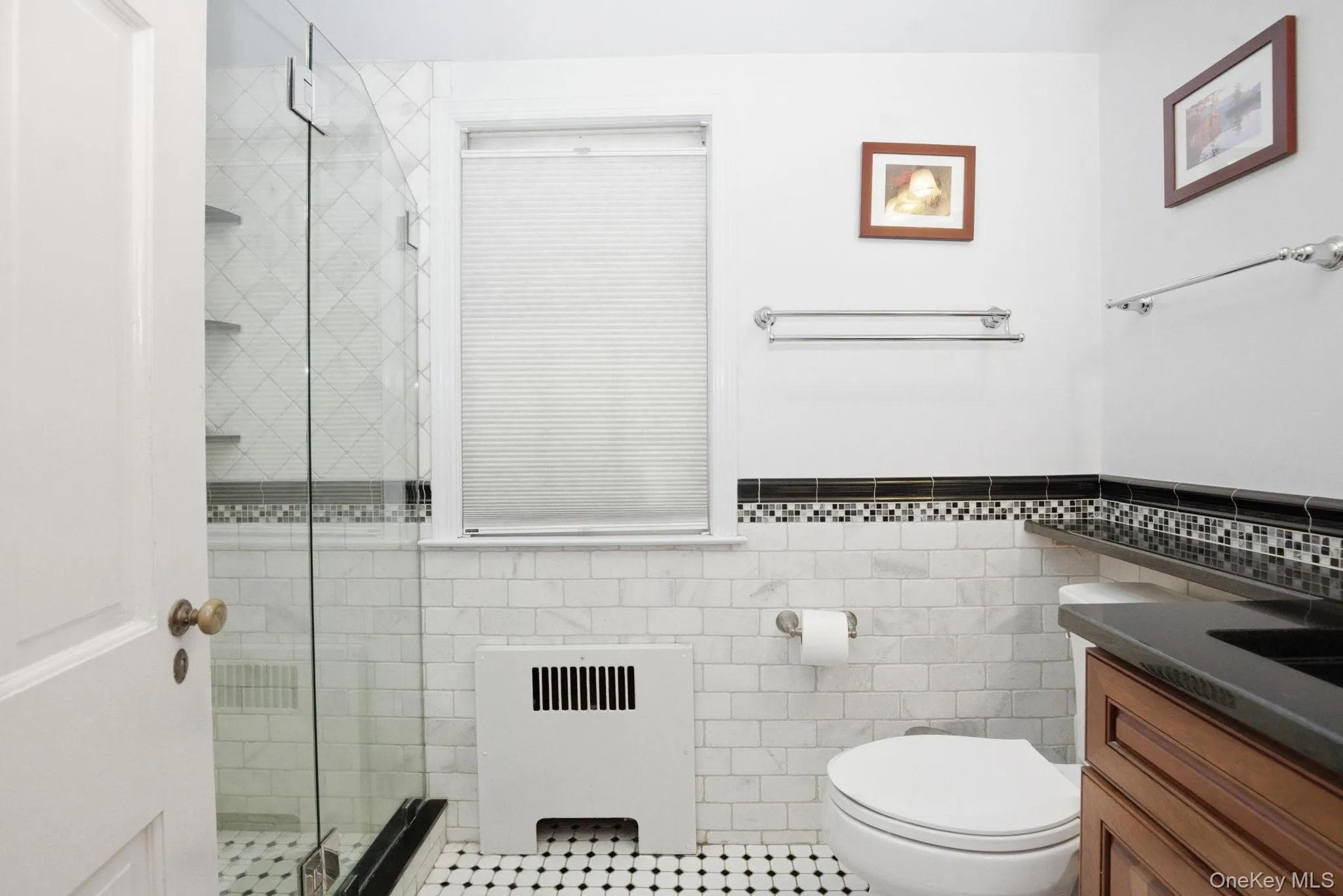 The renovated primary ensuite showcases marble tile wainscoting, a granite vanity, and classic black and white floor tile. The renovated primary ensuite showcases marble tile wainscoting, a granite vanity, and classic black and white floor tile.