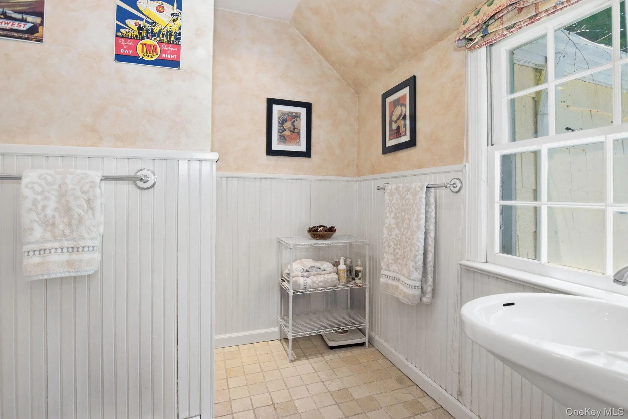 First-floor ensuite full bath featuring beadboard wainscoting, vaulted ceiling, and a window for natural light. First-floor ensuite full bath featuring beadboard wainscoting, vaulted ceiling, and a window for natural light.