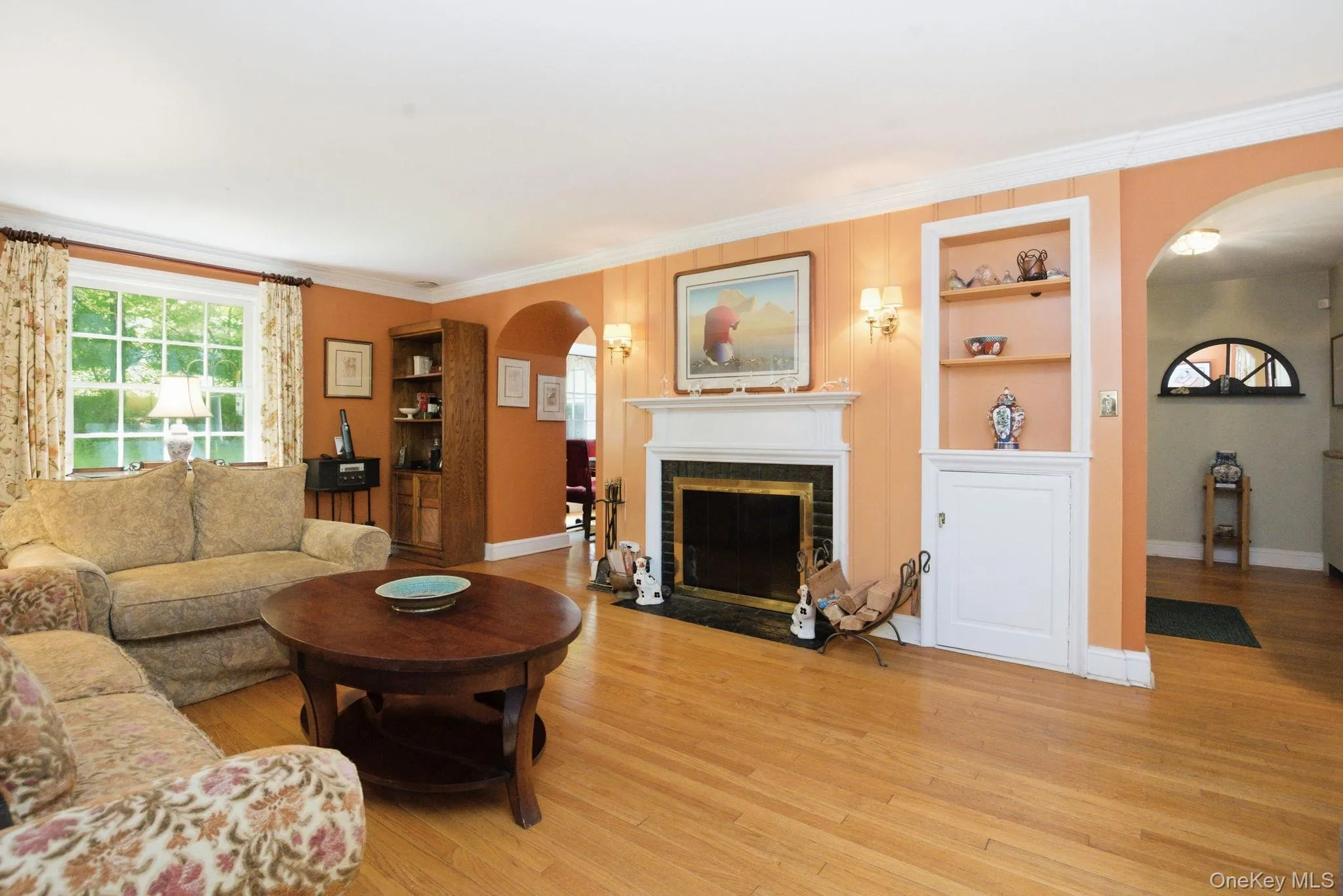 The living room features original hardwood floors, a wood-burning fireplace, and built-in shelving flanked by arched doorways. The living room features original hardwood floors, a wood-burning fireplace, and built-in shelving flanked by arched doorways.