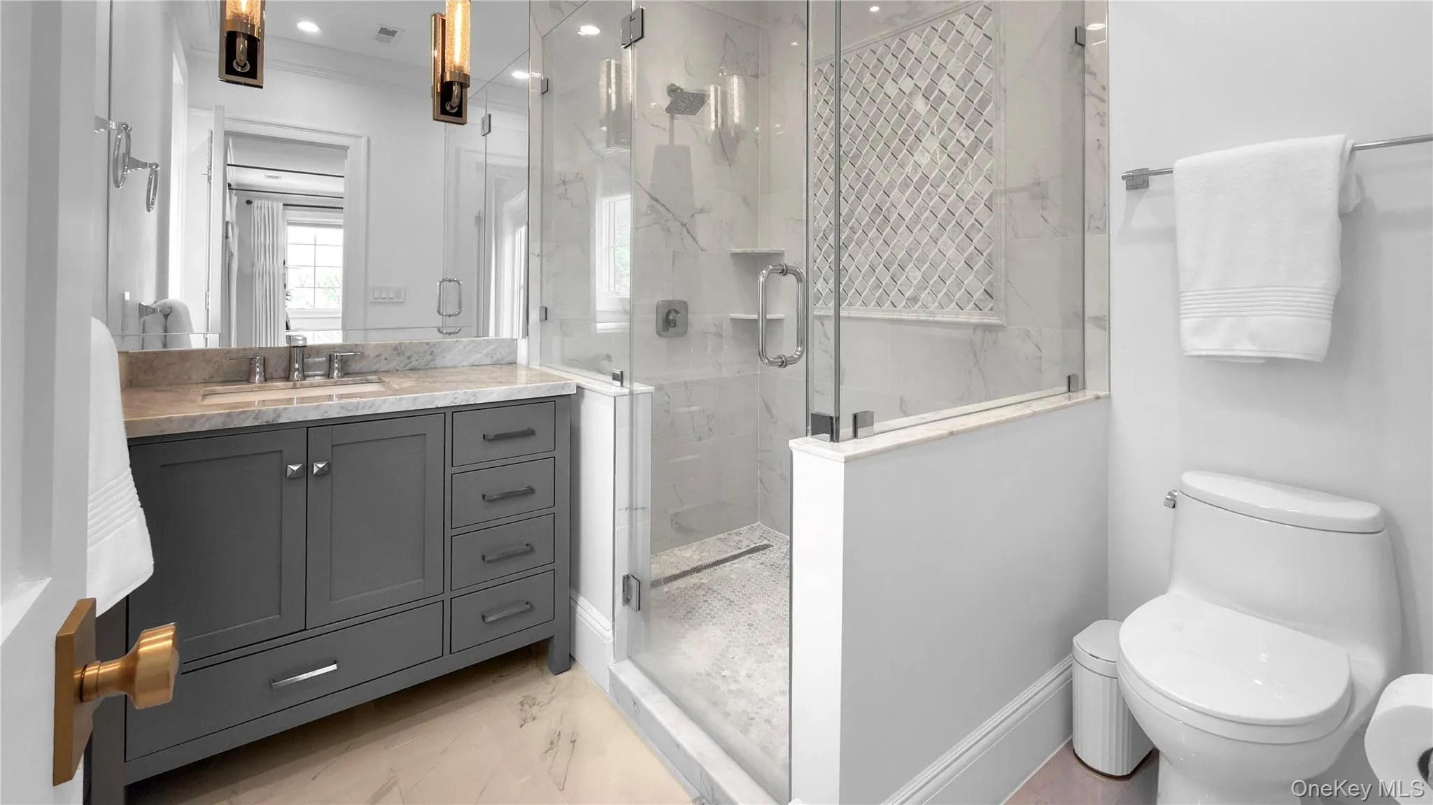 Contemporary bathroom featuring a spacious glass-enclosed shower with a decorative tile accent wall, a dark gray vanity with extensive storage, a light-toned countertop, and modern lighting fixtures Contemporary bathroom featuring a spacious glass-enclosed shower with a decorative tile accent wall, a dark gray vanity with extensive storage, a light-toned countertop, and modern lighting fixtures