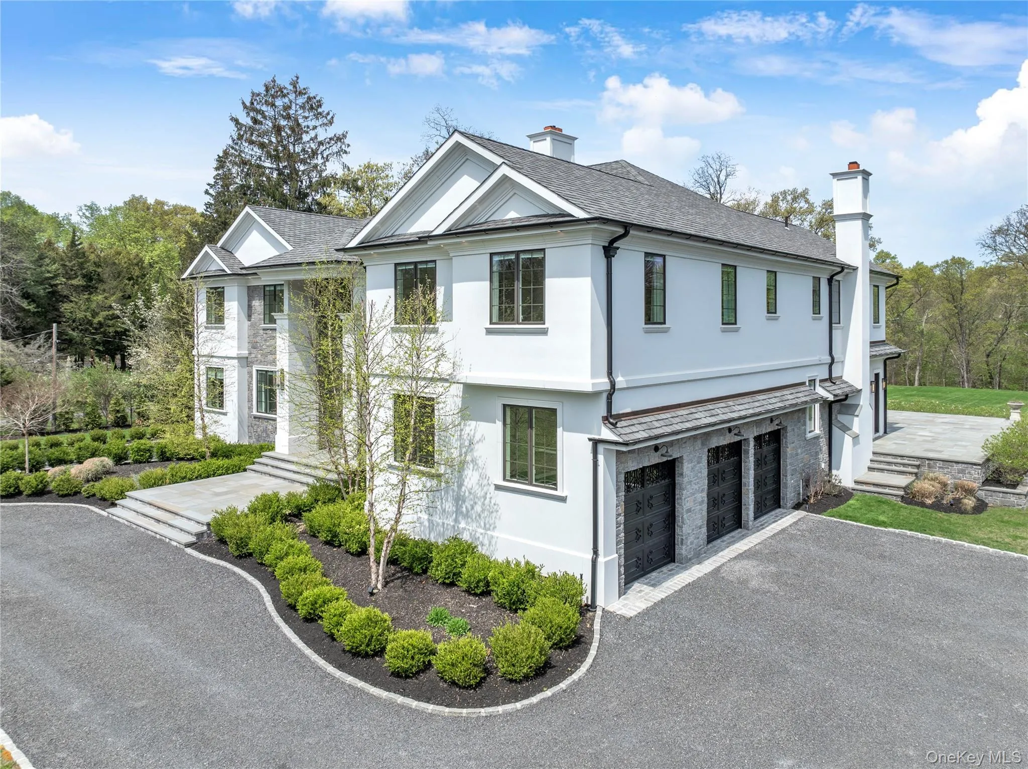 Contemporary stucco and stone exterior featuring a three-car garage, multiple gables, and a prominent chimney Contemporary stucco and stone exterior featuring a three-car garage, multiple gables, and a prominent chimney