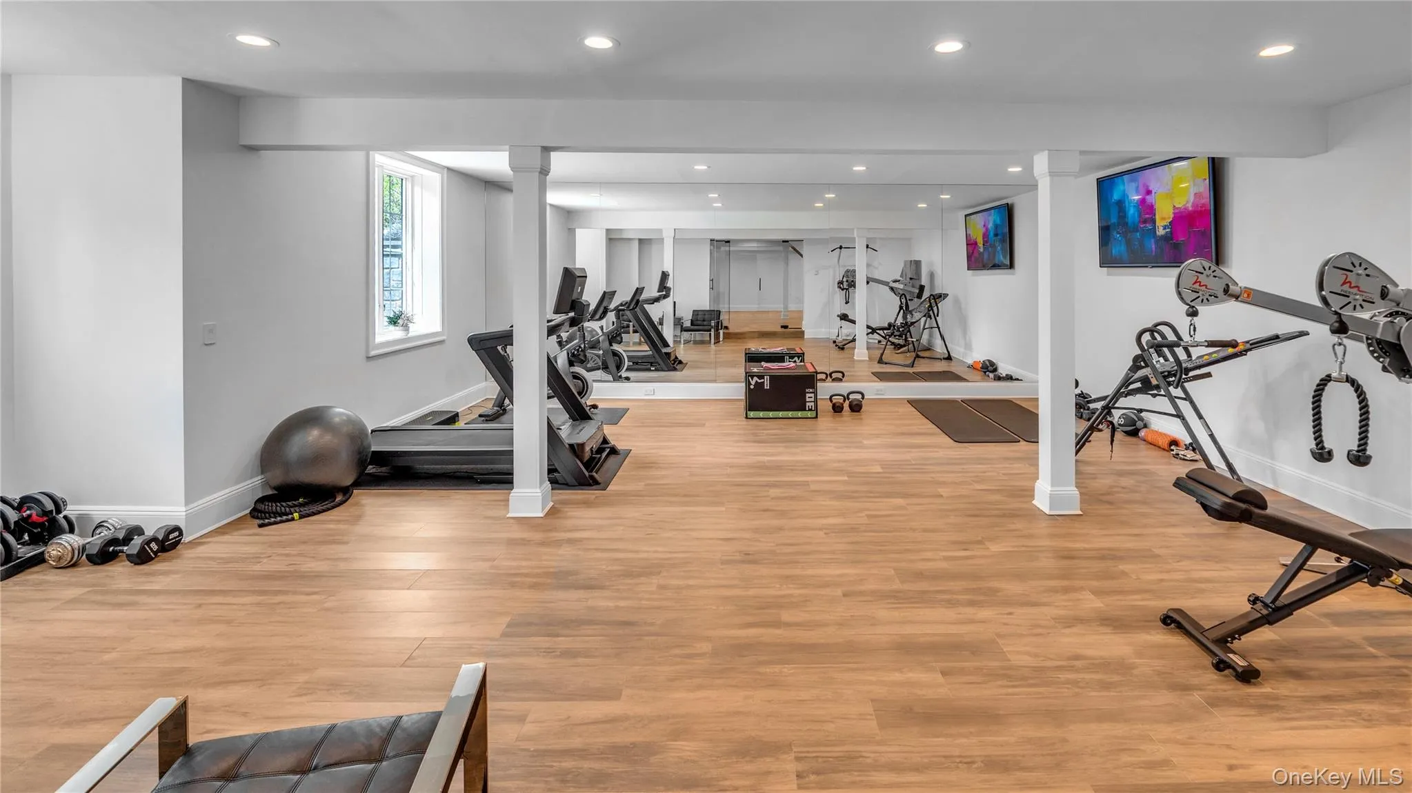 Dedicated fitness space featuring wood-finish flooring, recessed lighting, and mirrored walls Dedicated fitness space featuring wood-finish flooring, recessed lighting, and mirrored walls