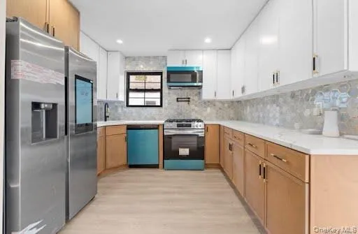 Modern kitchen featuring a stainless steel refrigerator, white upper cabinetry, natural wood-finish lower cabinetry, white countertops, and a patterned tile backsplash Modern kitchen featuring a stainless steel refrigerator, white upper cabinetry, natural wood-finish lower cabinetry, white countertops, and a patterned tile backsplash