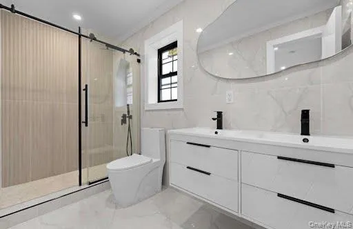 master bathroom featuring a dual vanity with undermount sinks and matte black fixtures, a frameless glass shower enclosure with a barn door style hardware, and floor-to-ceiling marble-look tile master bathroom featuring a dual vanity with undermount sinks and matte black fixtures, a frameless glass shower enclosure with a barn door style hardware, and floor-to-ceiling marble-look tile