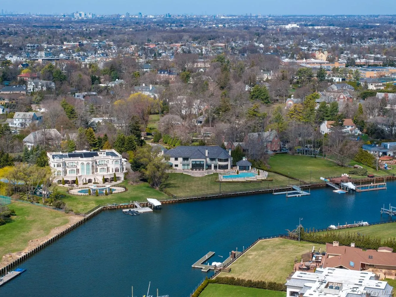 Waterfront estate featuring a grand facade, manicured lawns, two distinct swimming pools, private docks, and a tennis court Waterfront estate featuring a grand facade, manicured lawns, two distinct swimming pools, private docks, and a tennis court