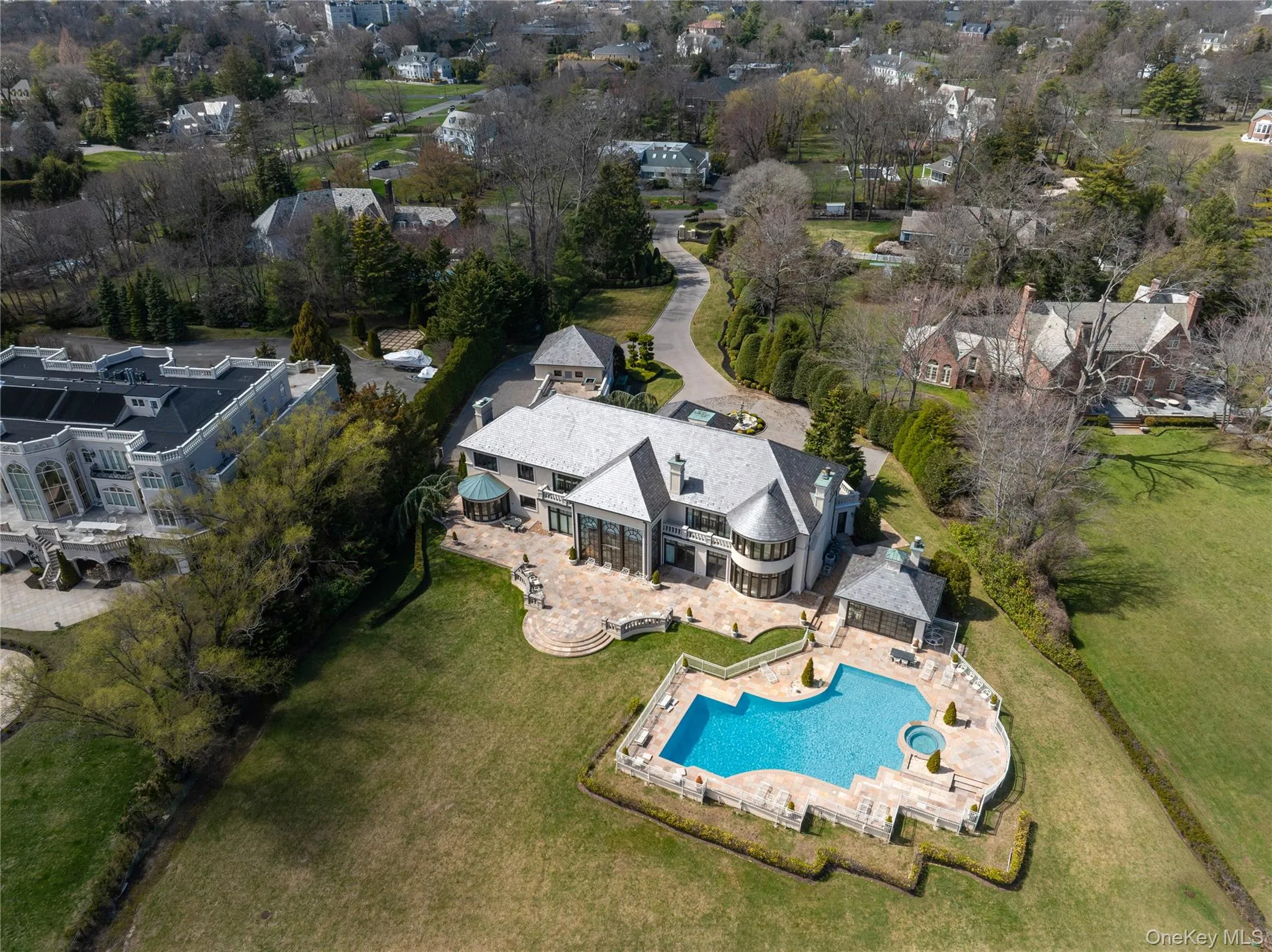 Expansive property featuring a large residence with a multi-level stone patio, a freeform swimming pool with an integrated spa, and a pool house Expansive property featuring a large residence with a multi-level stone patio, a freeform swimming pool with an integrated spa, and a pool house