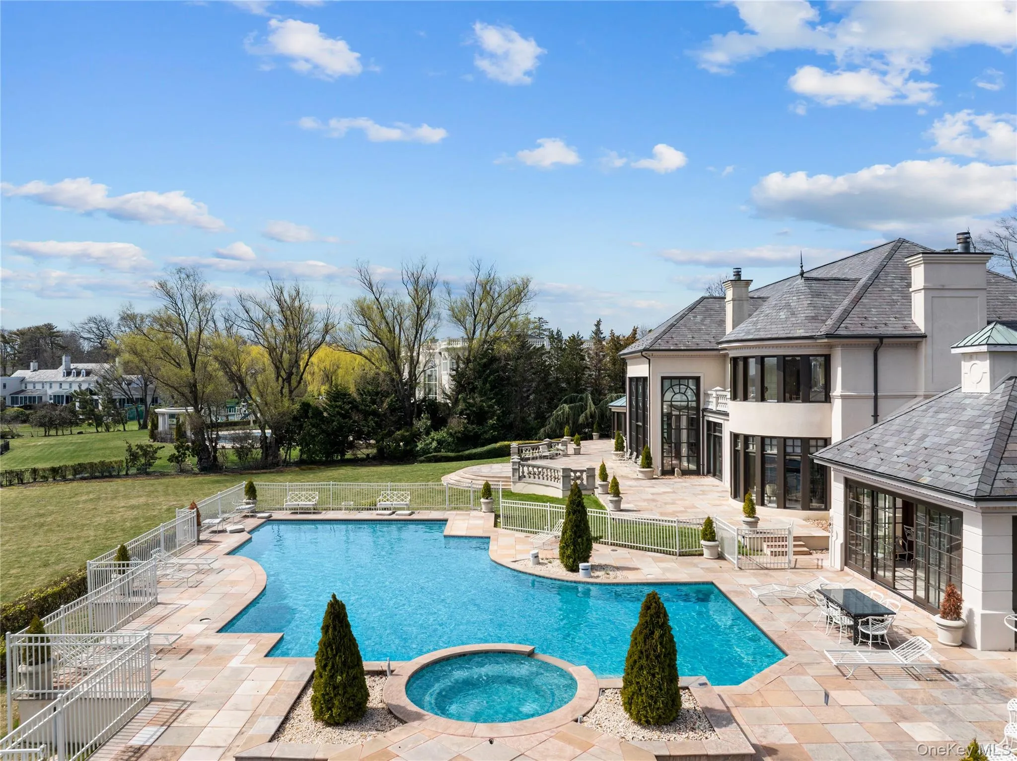 Expansive outdoor living area featuring a custom-shaped swimming pool with an integrated spa, set within a spacious stone patio Expansive outdoor living area featuring a custom-shaped swimming pool with an integrated spa, set within a spacious stone patio