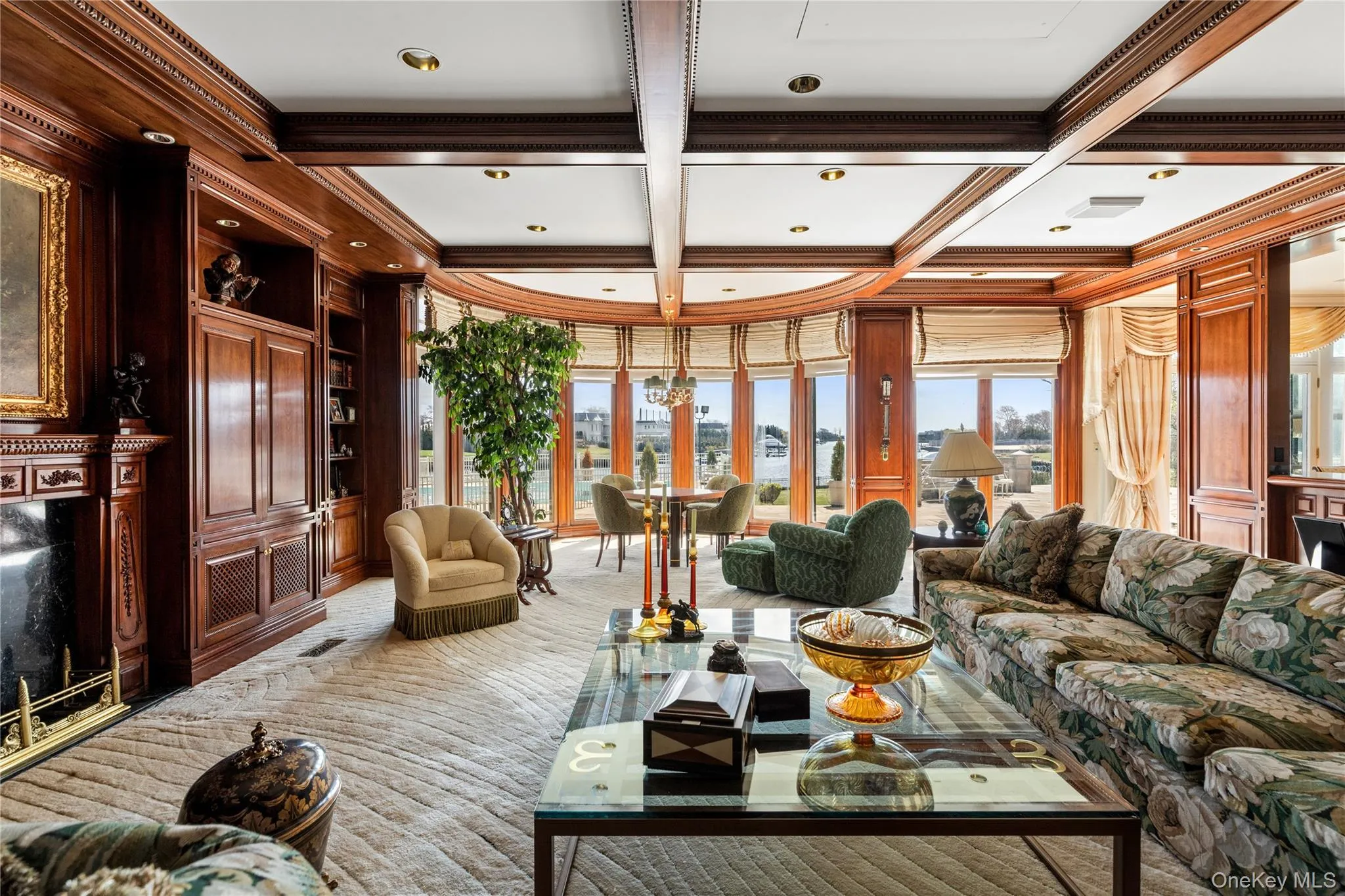 Expansive living area with intricate wood paneling, coffered ceiling, built-in cabinetry, and a fireplace featuring a dark stone surround Expansive living area with intricate wood paneling, coffered ceiling, built-in cabinetry, and a fireplace featuring a dark stone surround