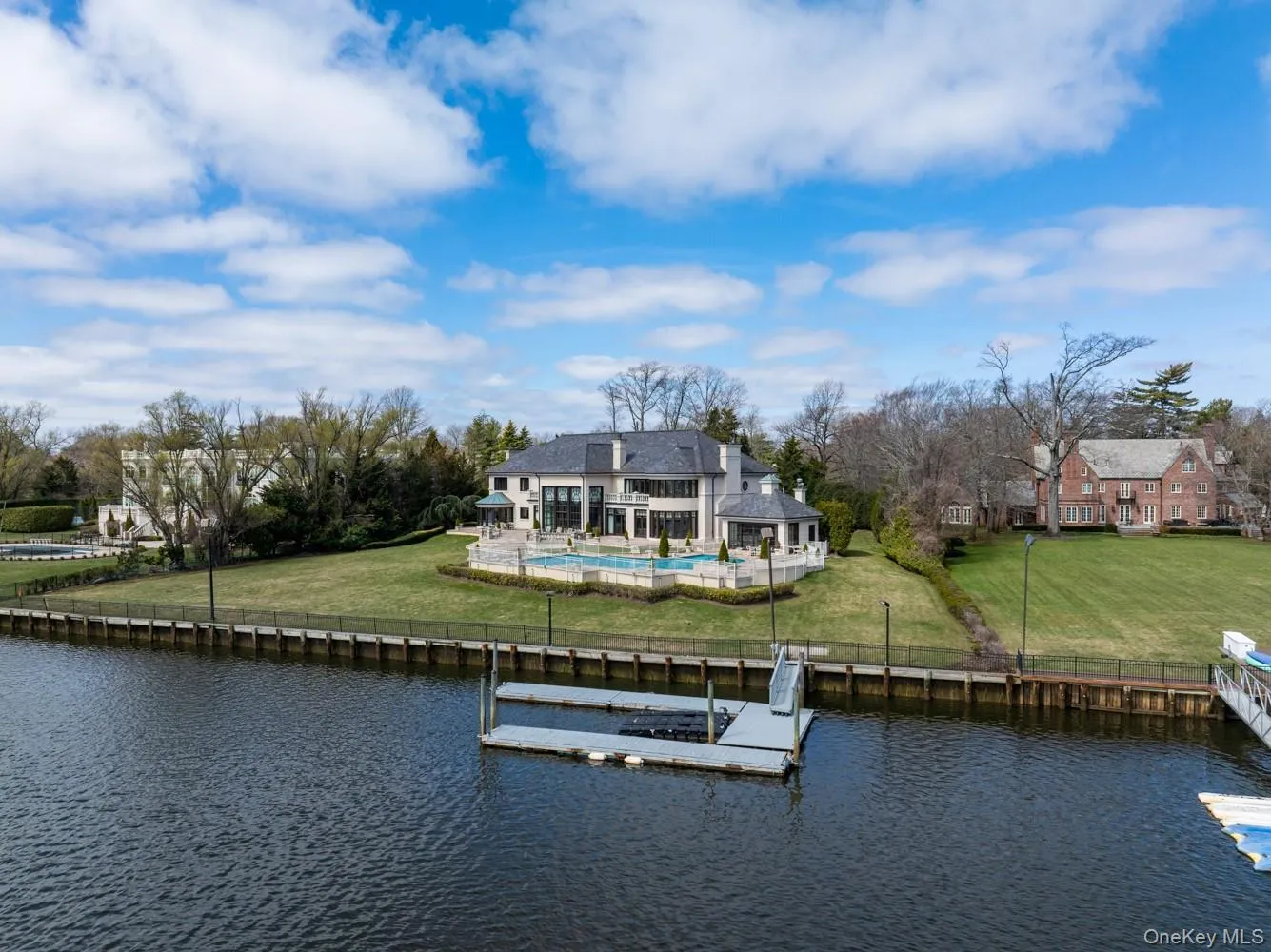Waterfront property featuring a substantial residence with a dark-tiled roof and light-toned exterior Waterfront property featuring a substantial residence with a dark-tiled roof and light-toned exterior