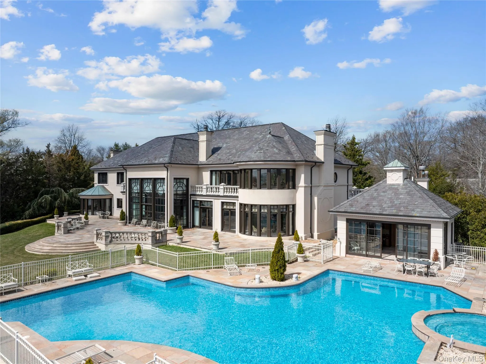 Sprawling outdoor entertaining space featuring a multi-level patio, a large swimming pool with integrated spa, and a pool house with sliding glass doors Sprawling outdoor entertaining space featuring a multi-level patio, a large swimming pool with integrated spa, and a pool house with sliding glass doors