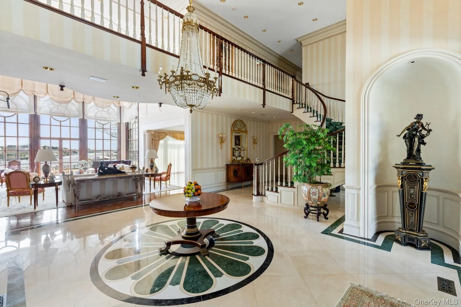 Grand foyer featuring polished tile flooring with a decorative inlay, an ornate chandelier, and a curved staircase with a dark wood handrail Grand foyer featuring polished tile flooring with a decorative inlay, an ornate chandelier, and a curved staircase with a dark wood handrail