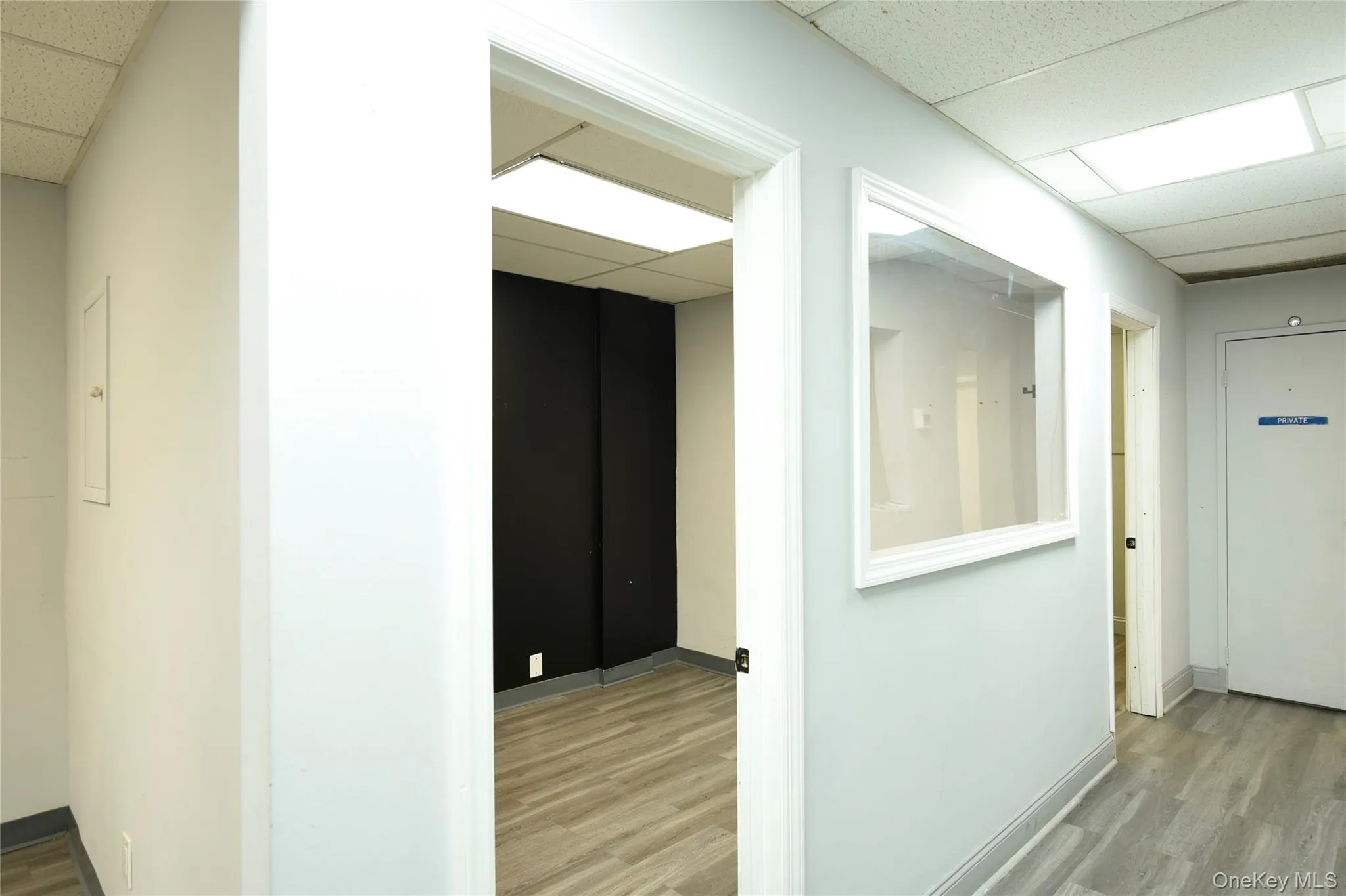 Hallway with wood-finish flooring, drop ceiling with integrated lighting, and a clear interior window Hallway with wood-finish flooring, drop ceiling with integrated lighting, and a clear interior window
