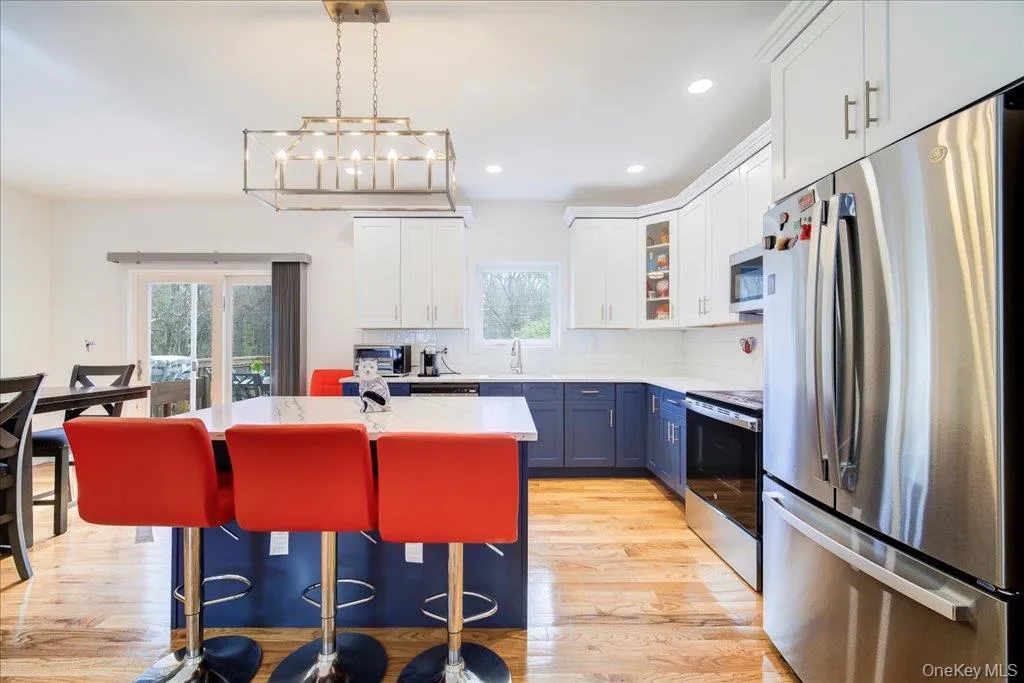 Kitchen featuring a two-tone cabinetry design with white upper and blue lower cabinets, stainless steel appliances, a center island with countertop seating, and wood-finish flooring Kitchen featuring a two-tone cabinetry design with white upper and blue lower cabinets, stainless steel appliances, a center island with countertop seating, and wood-finish flooring