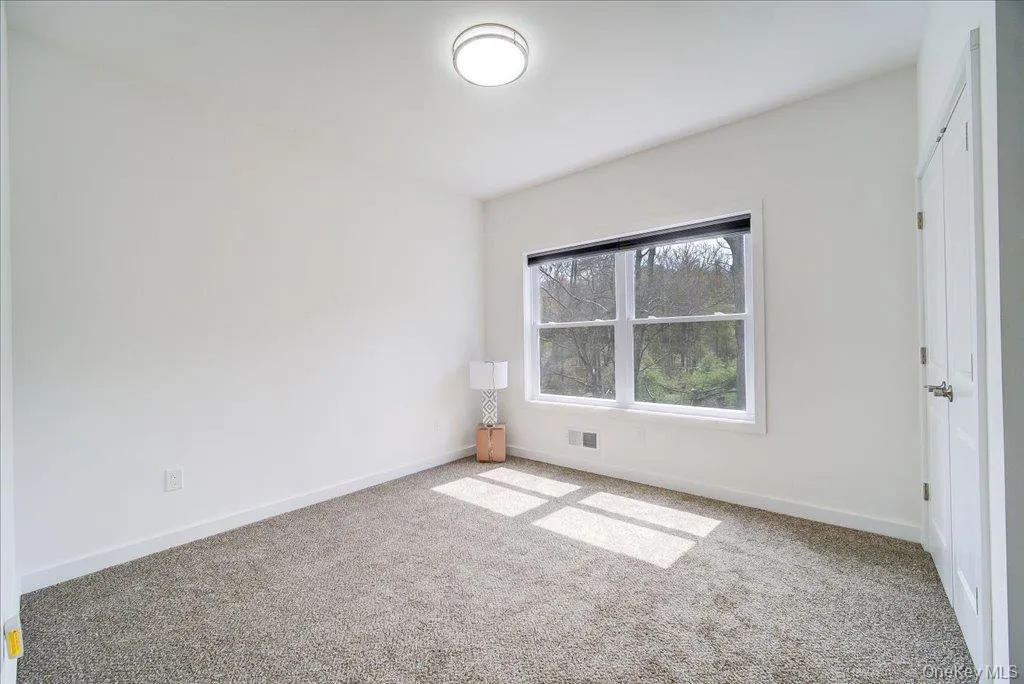 Carpeted room featuring a large window, a modern flush-mount ceiling light, white walls, and white trim Carpeted room featuring a large window, a modern flush-mount ceiling light, white walls, and white trim