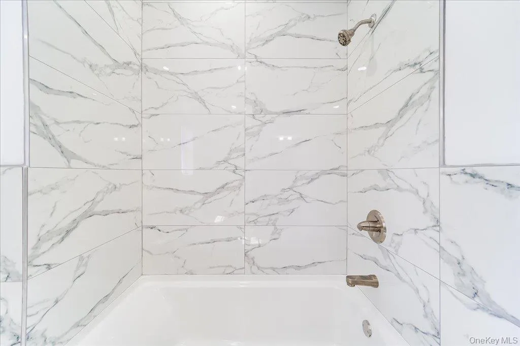 Bathtub and shower combination featuring large format marble-look tile surround and brushed nickel fixtures Bathtub and shower combination featuring large format marble-look tile surround and brushed nickel fixtures