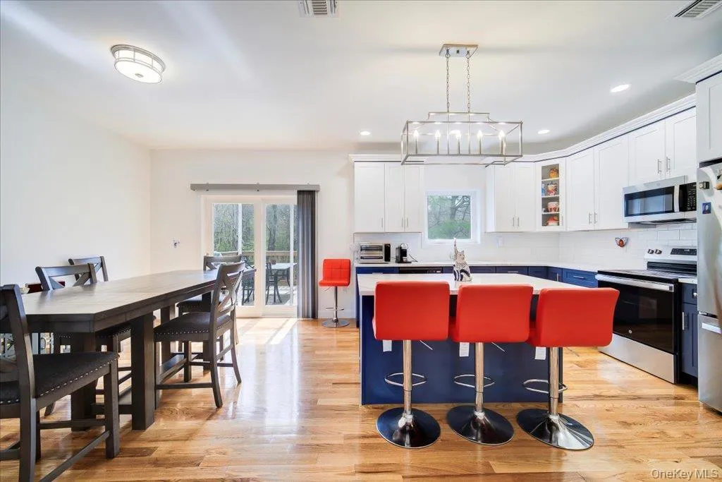 Open-concept kitchen with wood-finish flooring, a two-toned island, stainless steel appliances, white subway tile backsplash, and sliding glass doors Open-concept kitchen with wood-finish flooring, a two-toned island, stainless steel appliances, white subway tile backsplash, and sliding glass doors