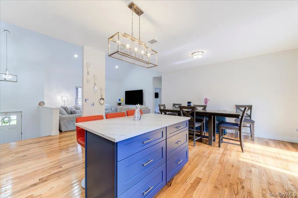 Kitchen island with a white countertop and blue cabinetry, hardwood flooring, and a dining area with a dark wood table Kitchen island with a white countertop and blue cabinetry, hardwood flooring, and a dining area with a dark wood table