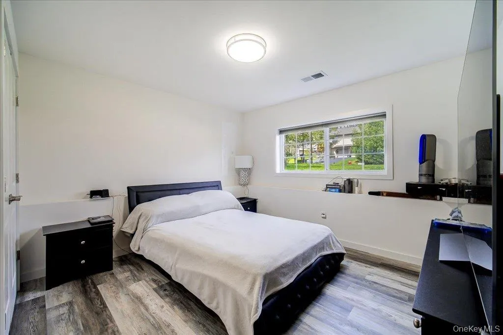 Bedroom featuring wood-finish flooring and a bright window with exterior landscaping Bedroom featuring wood-finish flooring and a bright window with exterior landscaping