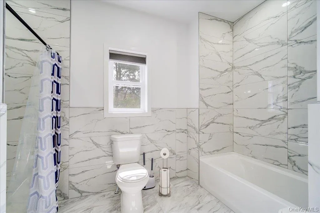 Bathroom featuring white-veined tile flooring and walls Bathroom featuring white-veined tile flooring and walls