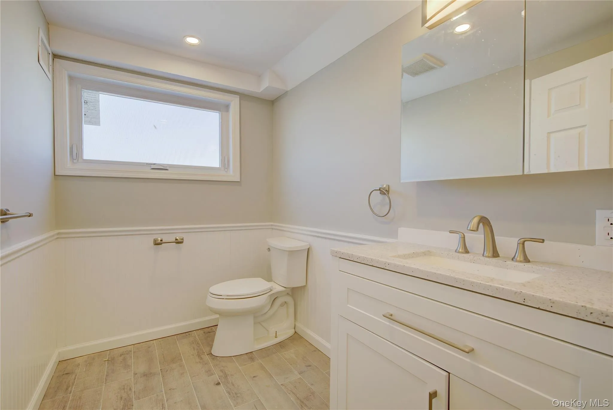 Half bath featuring vanity, toilet, wood finished floors, and a wainscoted wall Half bath featuring vanity, toilet, wood finished floors, and a wainscoted wall