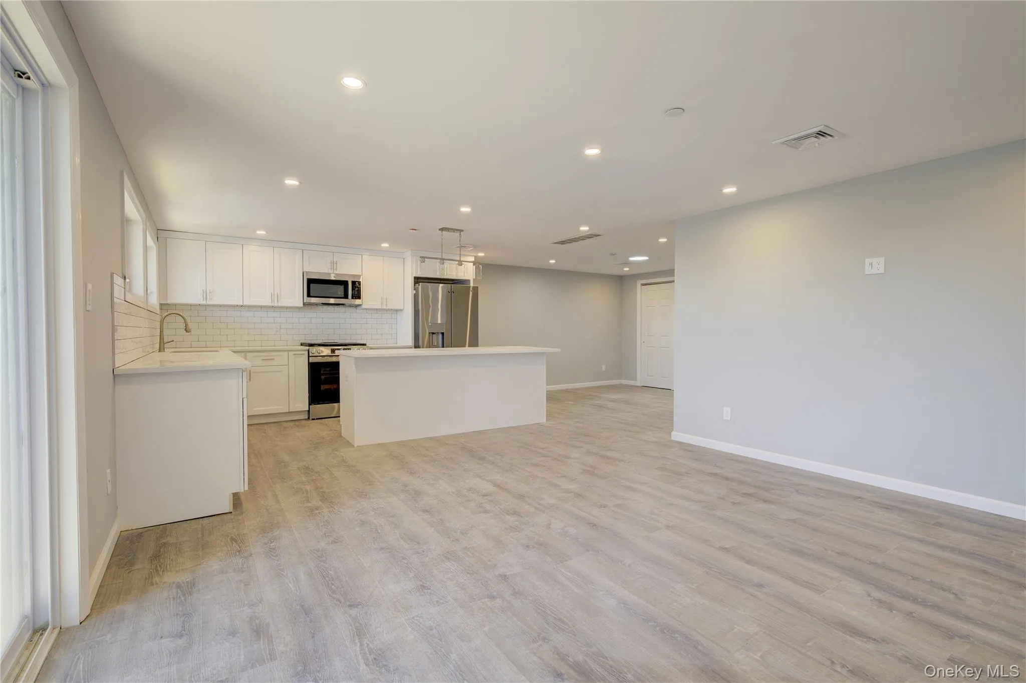 Kitchen featuring light wood-style flooring, backsplash, open floor plan, a center island, and appliances with stainless steel finishes Kitchen featuring light wood-style flooring, backsplash, open floor plan, a center island, and appliances with stainless steel finishes