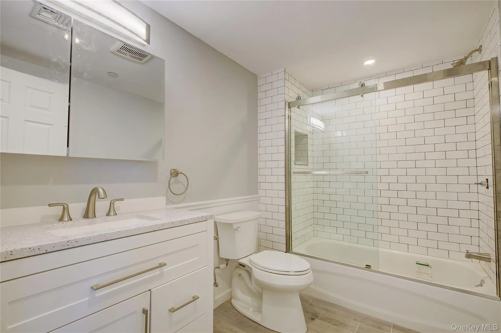 Full bathroom featuring vanity, wood finished floors, visible vents, shower / bath combination with glass door, and toilet Full bathroom featuring vanity, wood finished floors, visible vents, shower / bath combination with glass door, and toilet