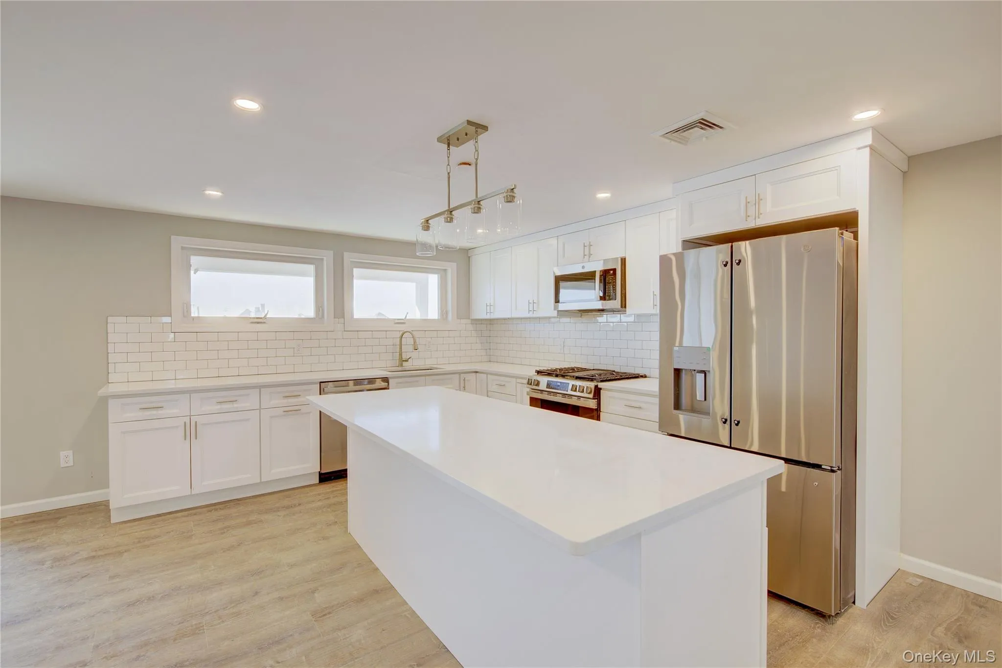 Kitchen with visible vents, white cabinets, light wood-style floors, appliances with stainless steel finishes, and tasteful backsplash Kitchen with visible vents, white cabinets, light wood-style floors, appliances with stainless steel finishes, and tasteful backsplash