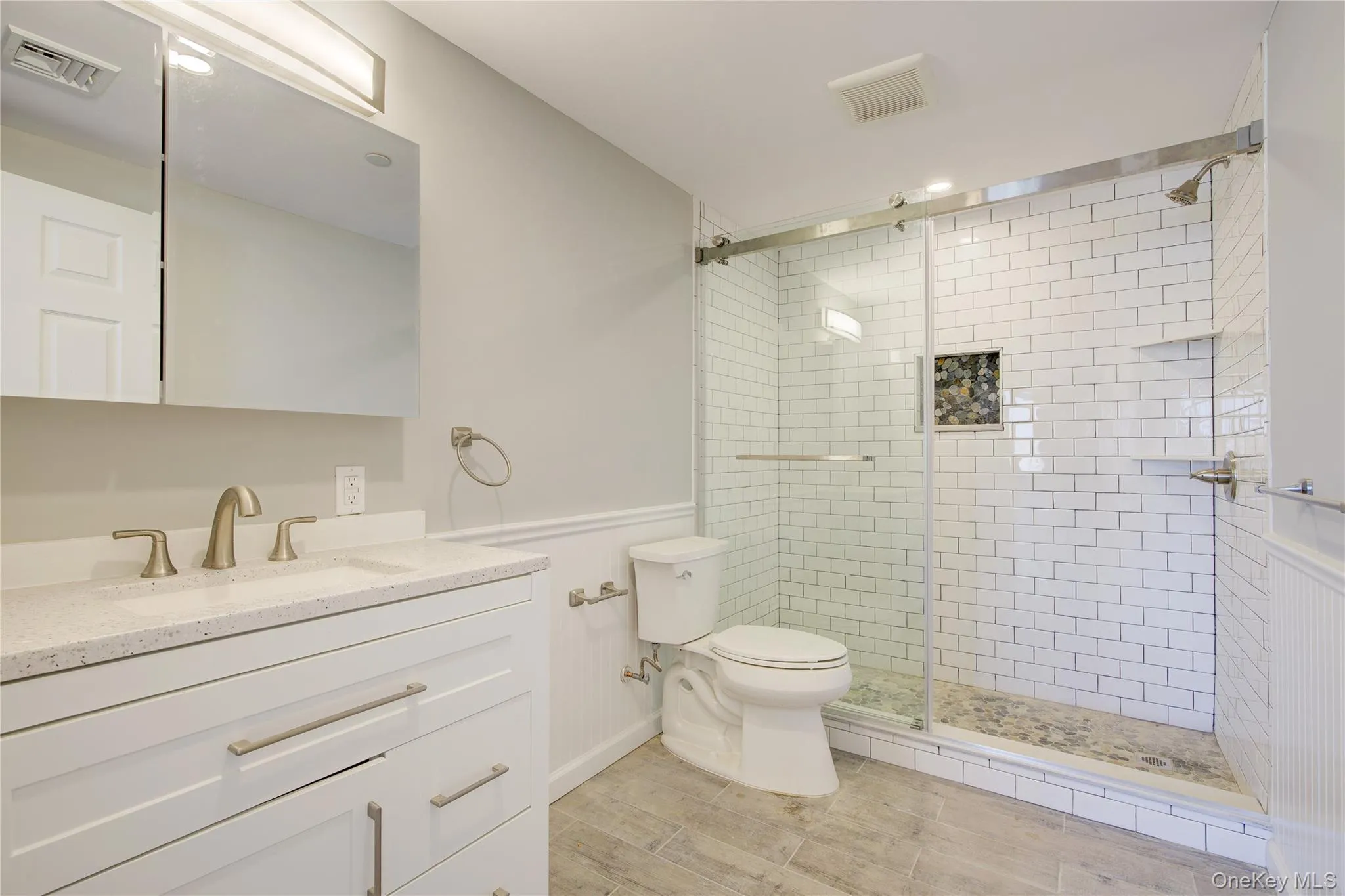 Bathroom featuring visible vents, toilet, a stall shower, wainscoting, and vanity Bathroom featuring visible vents, toilet, a stall shower, wainscoting, and vanity