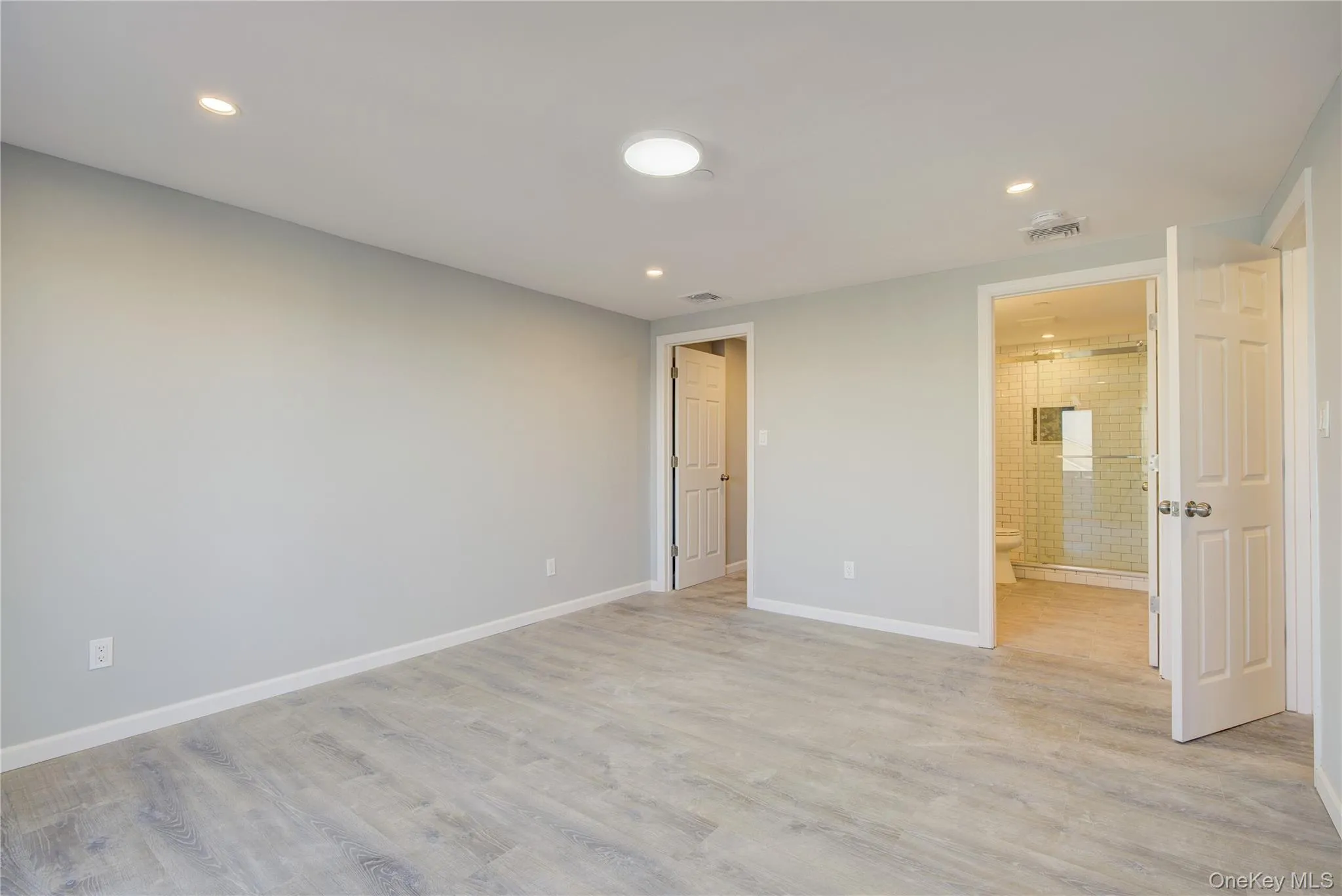 Unfurnished bedroom with visible vents, light wood-style flooring, ensuite bath, and baseboards Unfurnished bedroom with visible vents, light wood-style flooring, ensuite bath, and baseboards