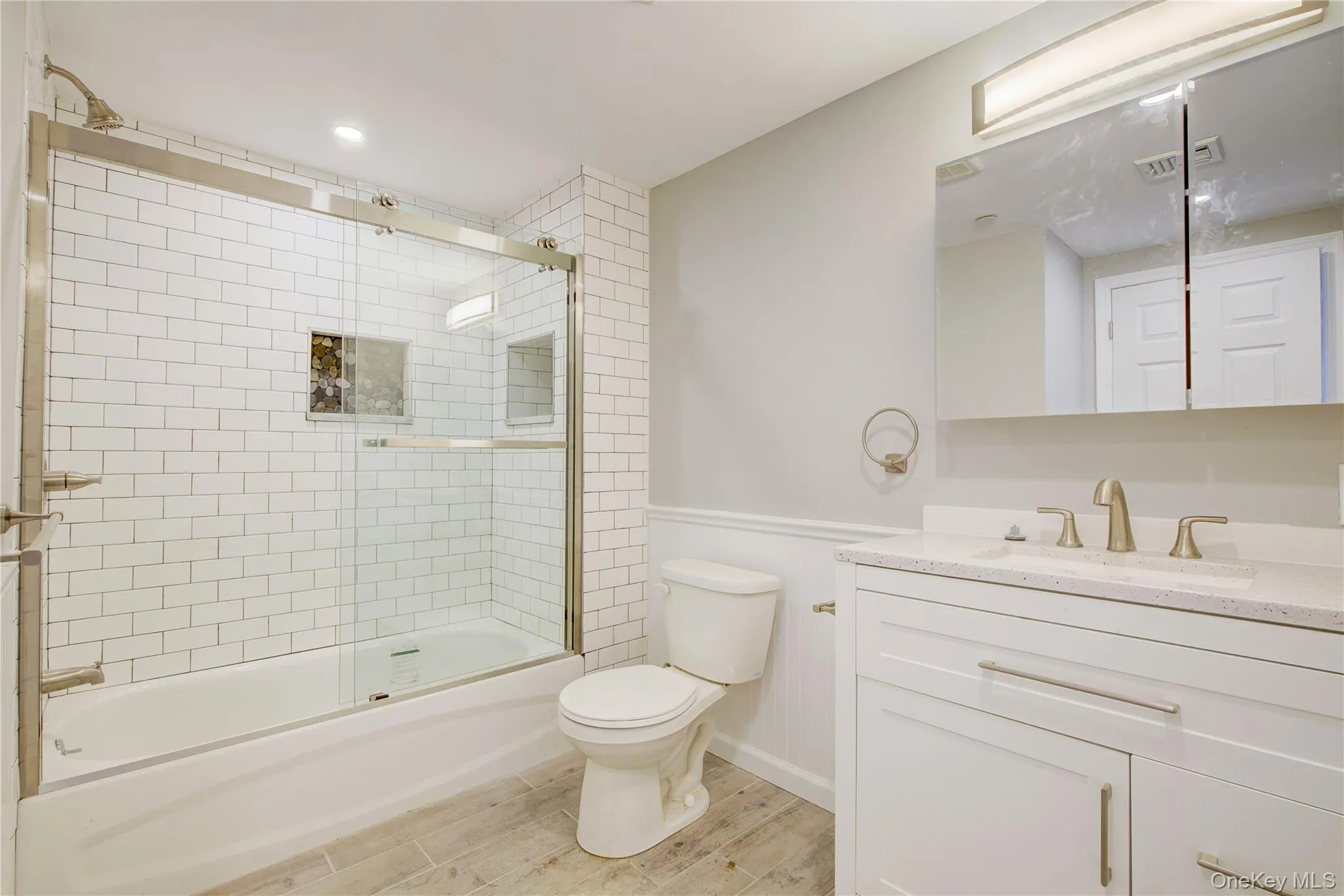 Bathroom featuring toilet, wood finished floors, combined bath / shower with glass door, baseboards, and vanity Bathroom featuring toilet, wood finished floors, combined bath / shower with glass door, baseboards, and vanity