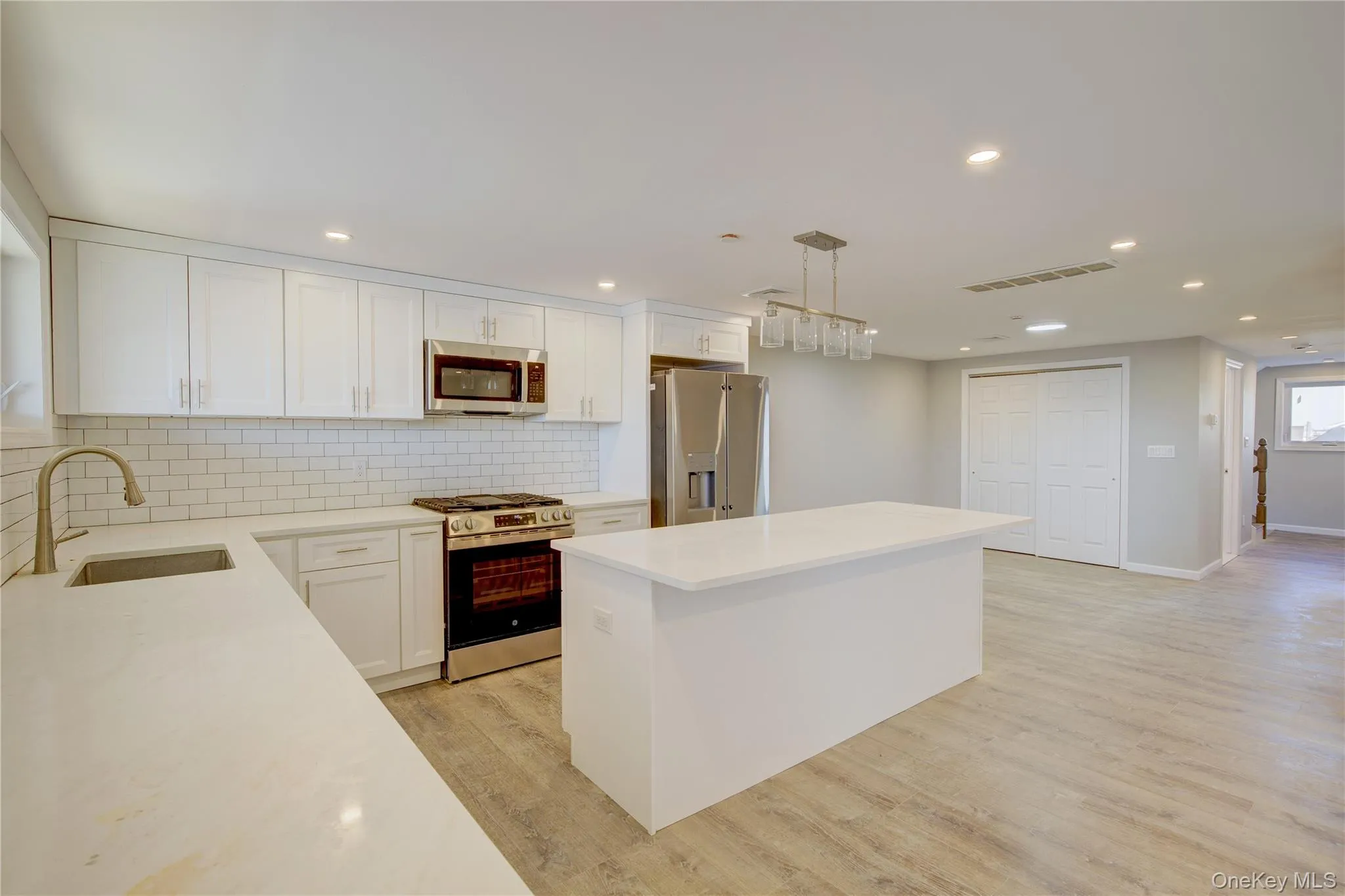 Kitchen featuring visible vents, light wood finished floors, a kitchen island, a sink, and stainless steel appliances Kitchen featuring visible vents, light wood finished floors, a kitchen island, a sink, and stainless steel appliances