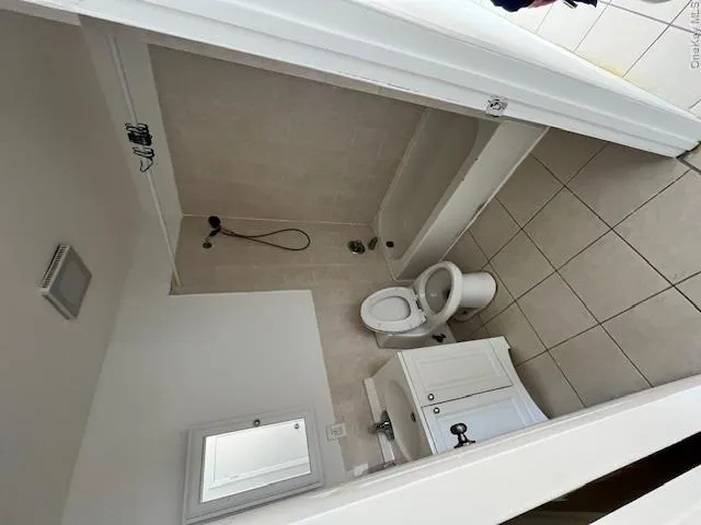 Bathroom featuring a white vanity with double doors, a mirror, a toilet, and a bathtub with an integrated shower Bathroom featuring a white vanity with double doors, a mirror, a toilet, and a bathtub with an integrated shower