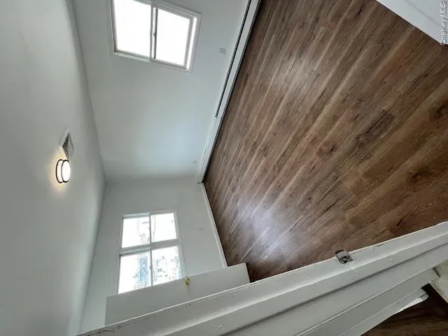 Spacious room featuring wood-finish flooring, white walls, two windows providing natural light, and a modern flush-mount ceiling light Spacious room featuring wood-finish flooring, white walls, two windows providing natural light, and a modern flush-mount ceiling light