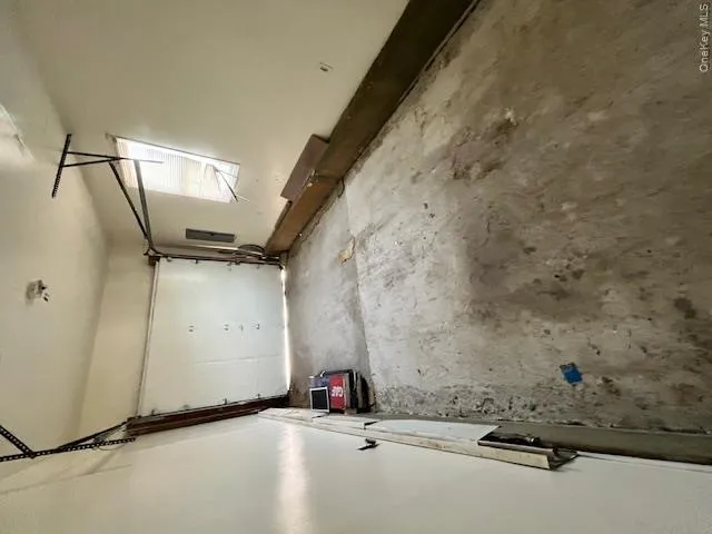 Single-car garage space with a roll-up door, exposed ceiling joists, and a side window Single-car garage space with a roll-up door, exposed ceiling joists, and a side window