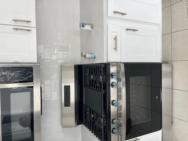 Modern kitchen featuring a stainless steel range with a griddle, white subway tile backsplash, white cabinetry with gold-tone hardware, and light-colored countertops Modern kitchen featuring a stainless steel range with a griddle, white subway tile backsplash, white cabinetry with gold-tone hardware, and light-colored countertops