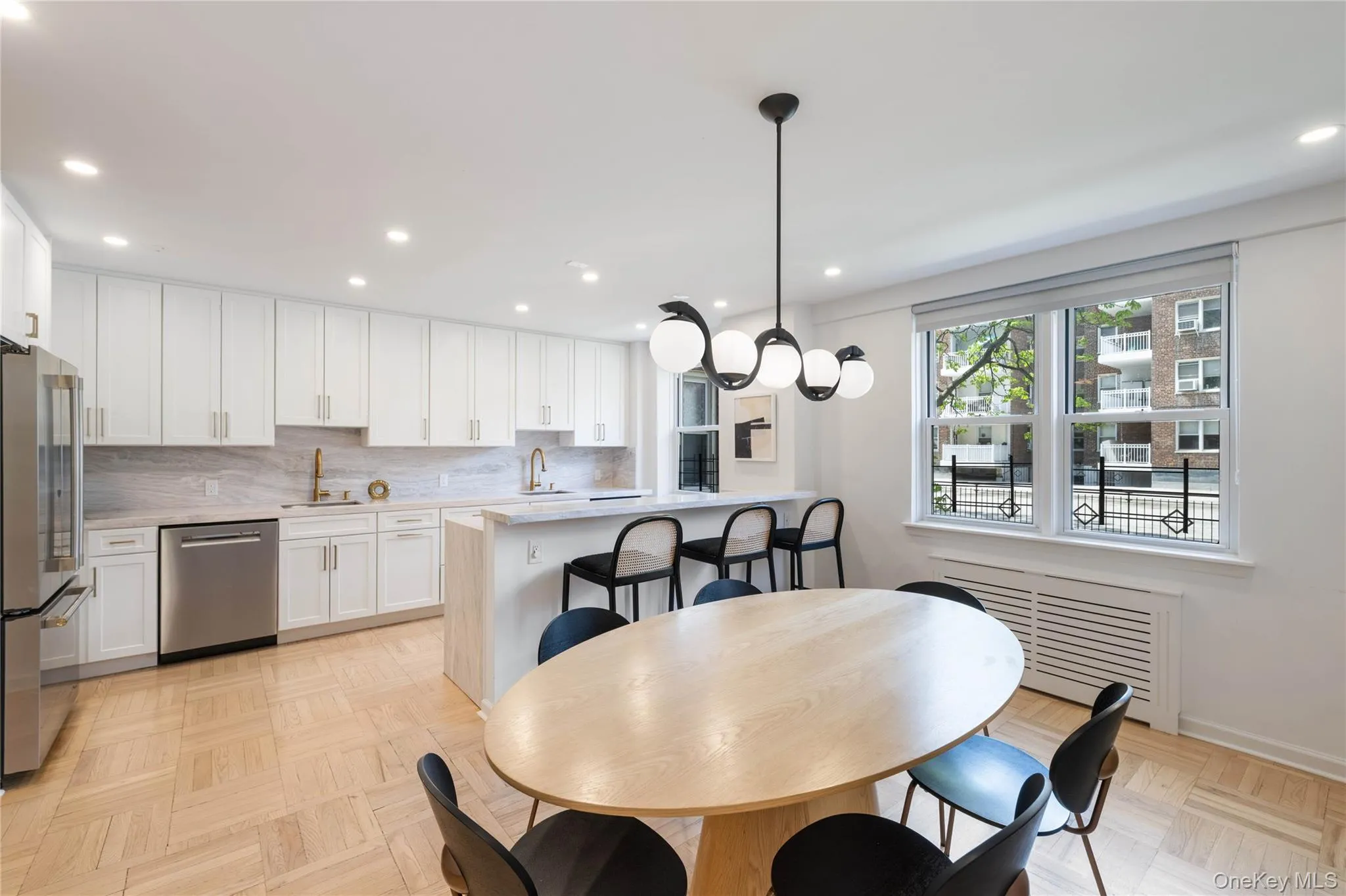 Open-concept kitchen and dining area featuring white shaker cabinetry, stainless steel appliances, a center island with bar seating, and parquet flooring Open-concept kitchen and dining area featuring white shaker cabinetry, stainless steel appliances, a center island with bar seating, and parquet flooring
