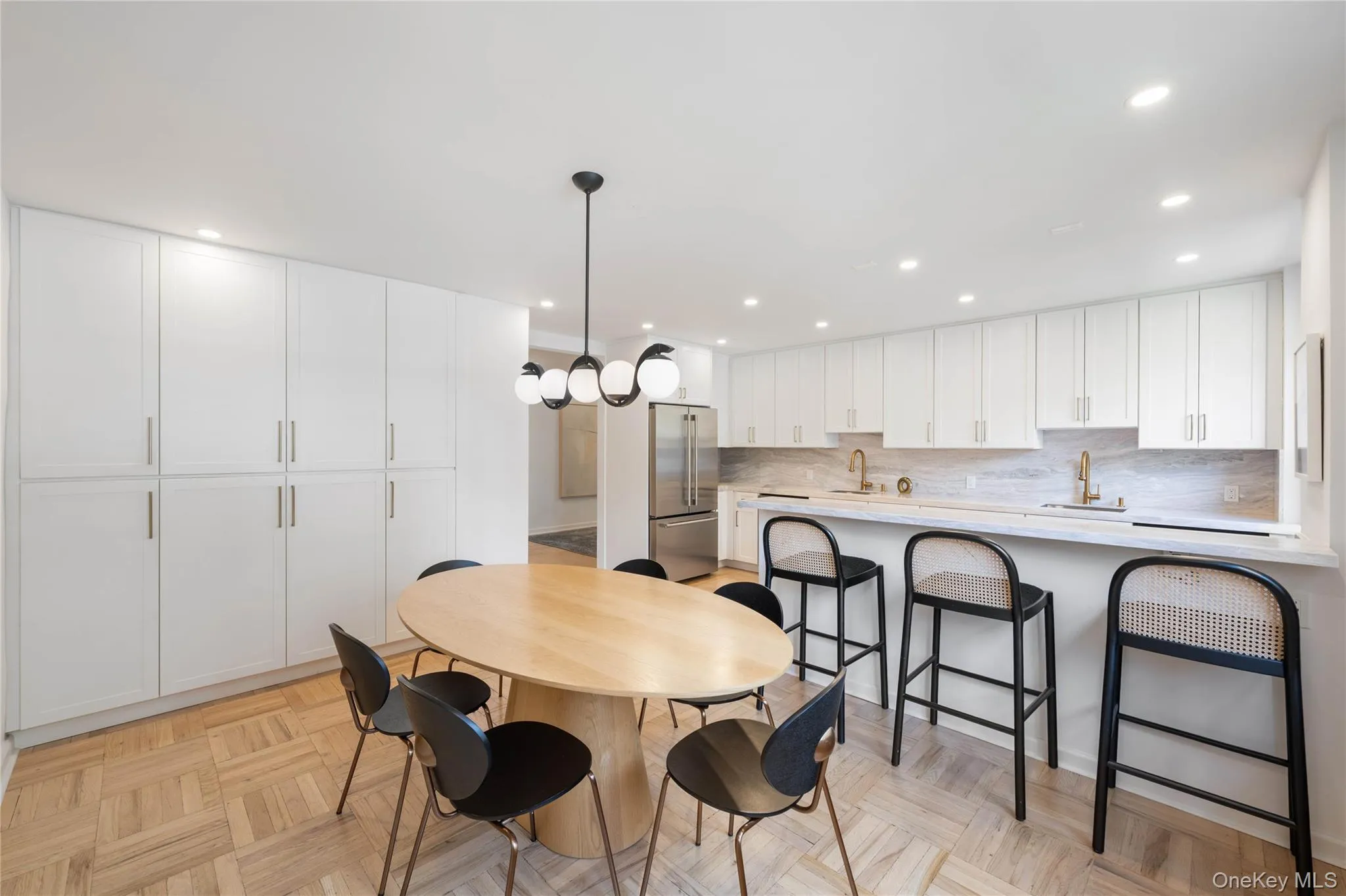 Open-concept kitchen and dining area featuring a full wall of white cabinetry, parquet wood flooring, recessed lighting, and a contemporary spherical chandelier Open-concept kitchen and dining area featuring a full wall of white cabinetry, parquet wood flooring, recessed lighting, and a contemporary spherical chandelier