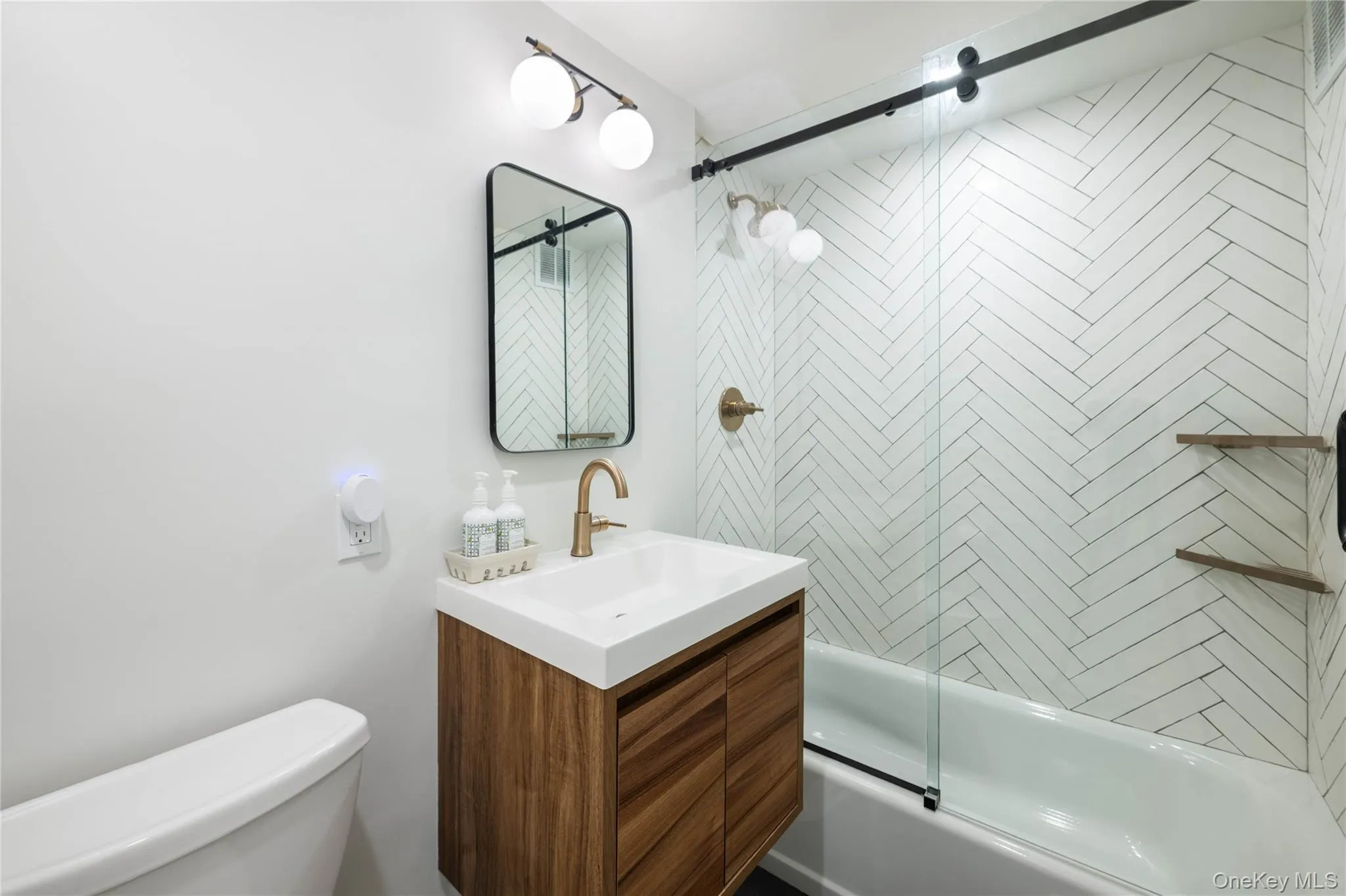 Bathroom featuring a wood vanity with a white rectangular sink, and a wall-mounted light fixture Bathroom featuring a wood vanity with a white rectangular sink, and a wall-mounted light fixture