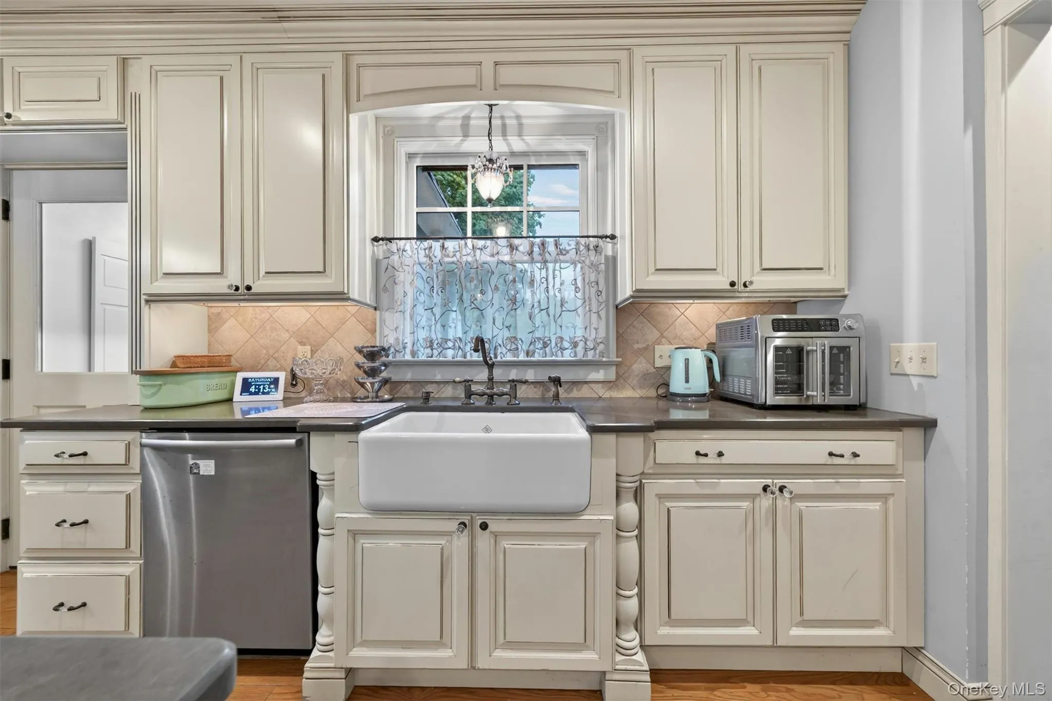 An oversize white Farmhouse sink accents stainless appliances in this bright kitchen modernized with both recessed lighting and vintage light fixtures... An oversize white Farmhouse sink accents stainless appliances in this bright kitchen modernized with both recessed lighting and vintage light fixtures...