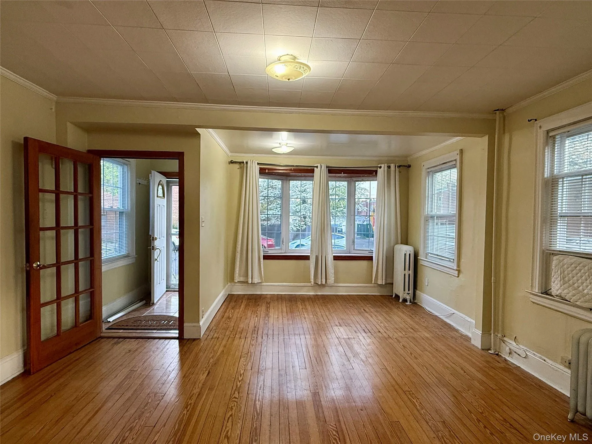 Open-concept living space with wood-finish flooring, multiple windows, and a French door entry Open-concept living space with wood-finish flooring, multiple windows, and a French door entry