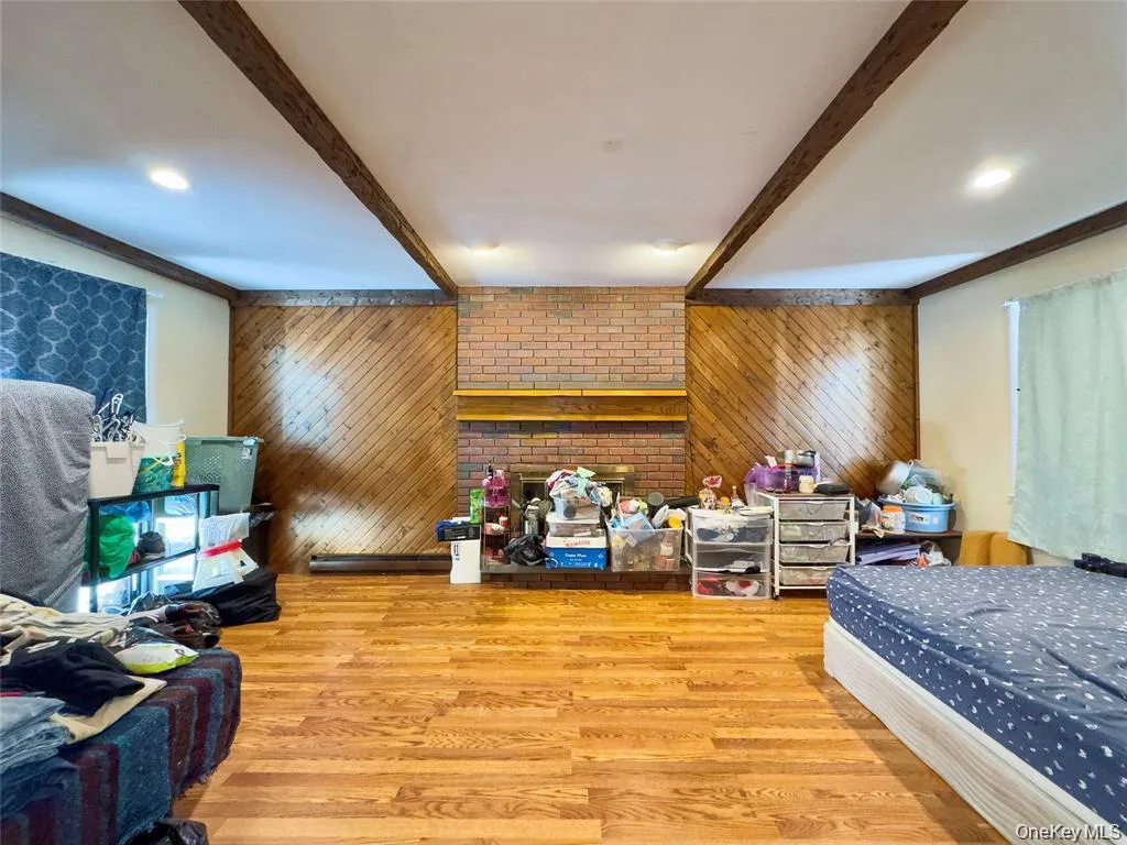 Spacious interior featuring wood-finish flooring, a brick fireplace with a wood mantel, diagonal wood paneling, exposed ceiling beams, and recessed lighting Spacious interior featuring wood-finish flooring, a brick fireplace with a wood mantel, diagonal wood paneling, exposed ceiling beams, and recessed lighting