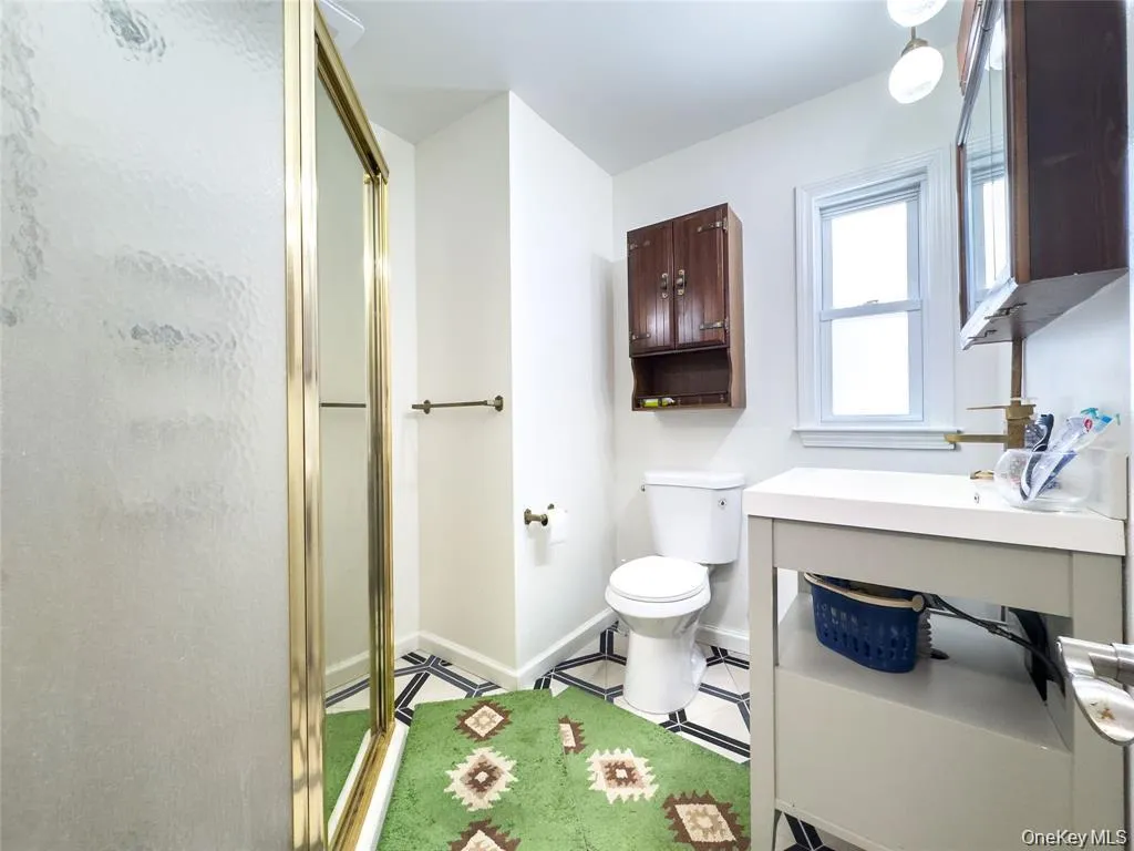 Bathroom featuring a gold-framed shower enclosure, white vanity with integrated sink, toilet, and patterned floor tile Bathroom featuring a gold-framed shower enclosure, white vanity with integrated sink, toilet, and patterned floor tile