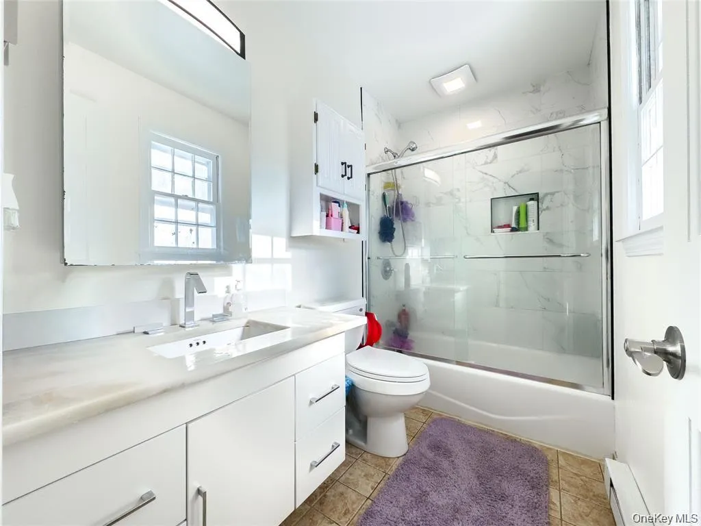Full bathroom featuring a single vanity with a solid surface countertop, white cabinetry with chrome hardware, and a shower-over-tub with sliding glass doors Full bathroom featuring a single vanity with a solid surface countertop, white cabinetry with chrome hardware, and a shower-over-tub with sliding glass doors